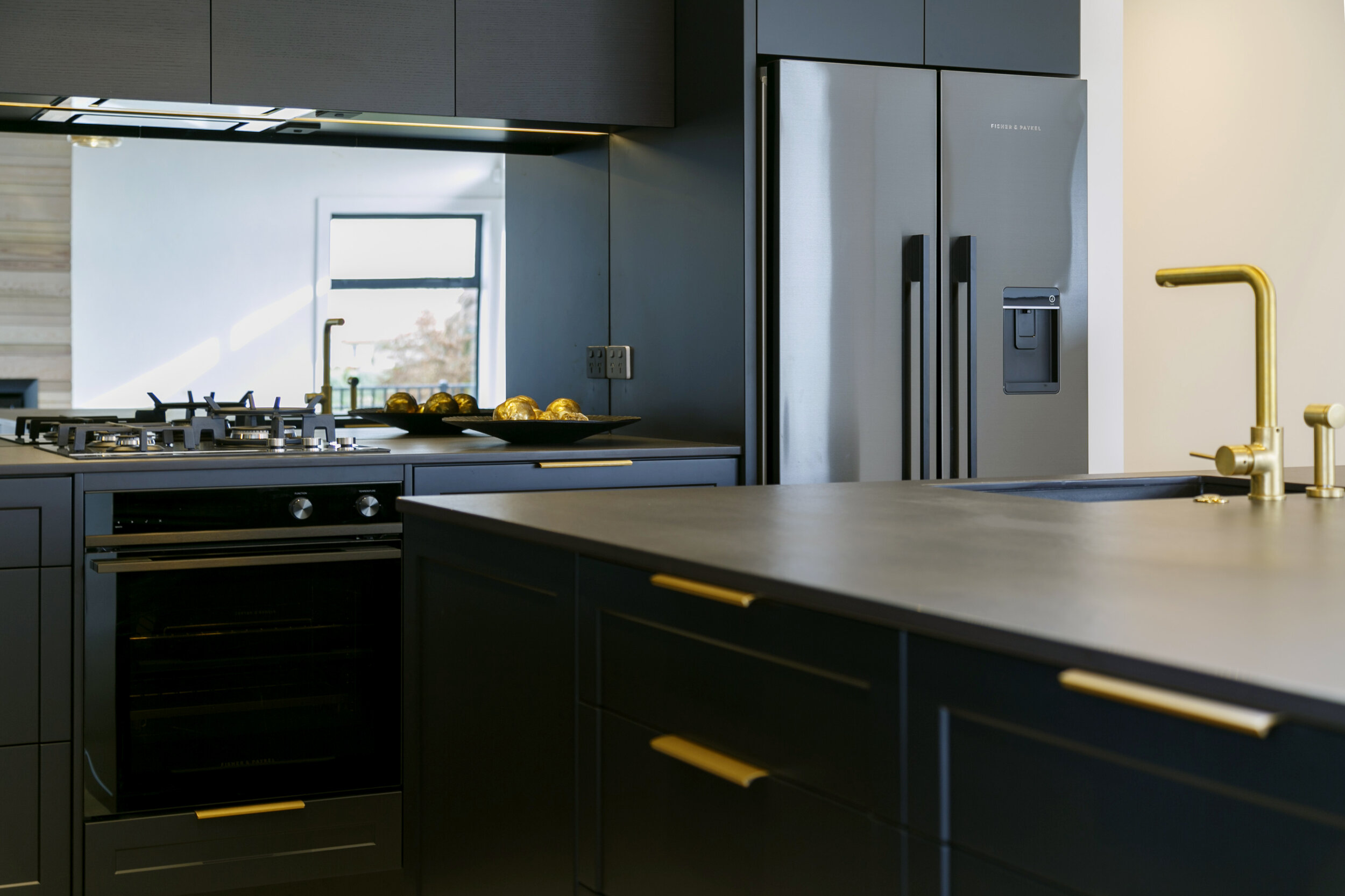 Dark mirror splashback in kitchen with dark cabinetry and gold handle and tap detail