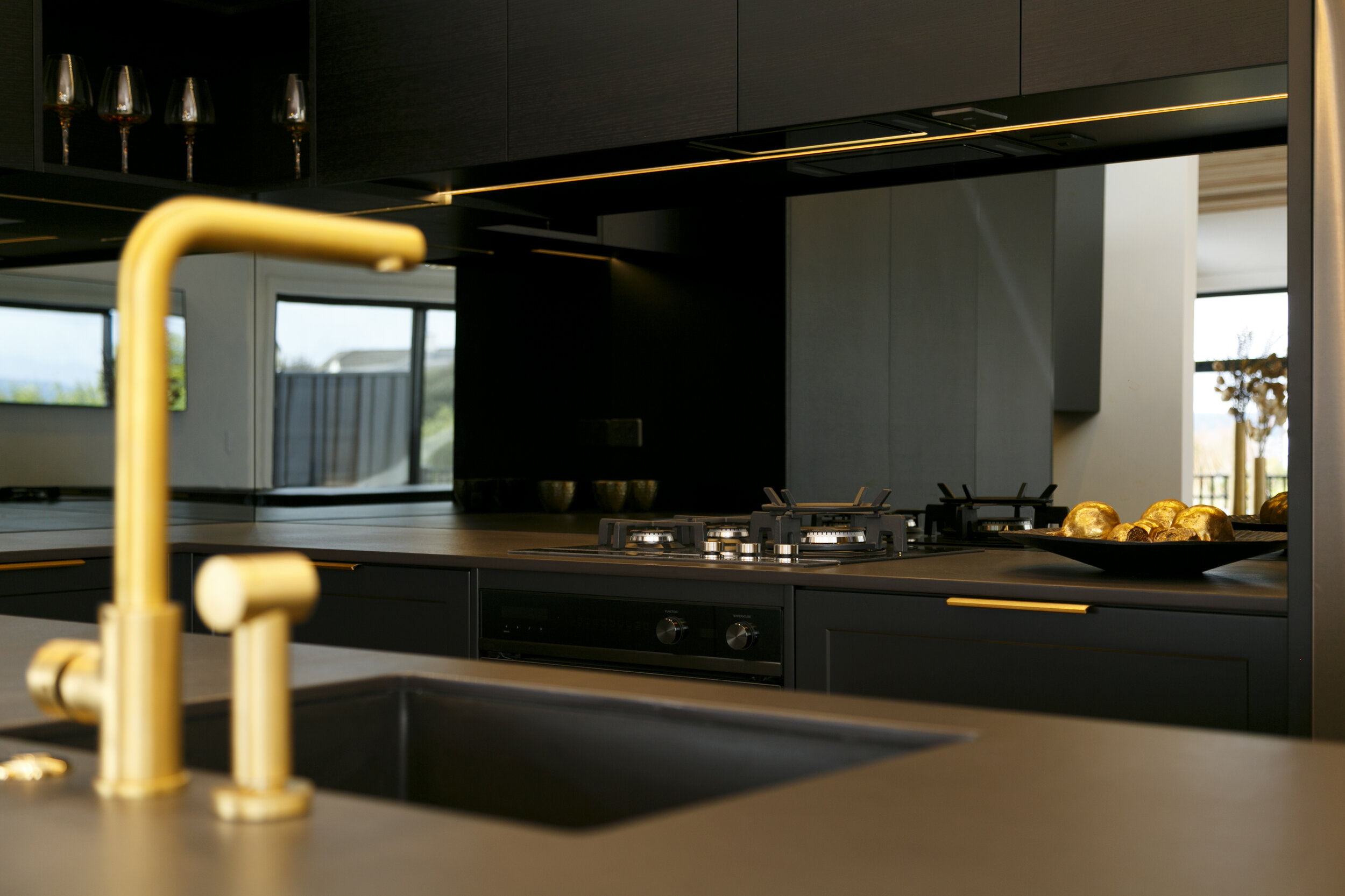 Gold tap and handles with dark mirror glass splashback