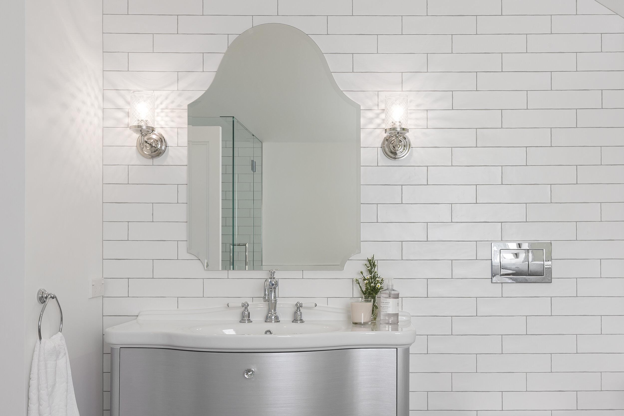 Shaped mirror on tiled wall in white bathroom with silver freestanding vanity