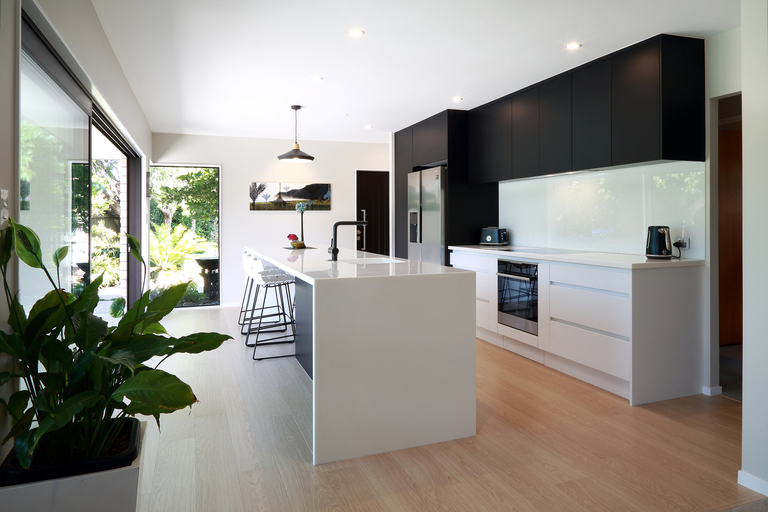 Waterfall end white stone island with dark cabinetry overhead cabinets and white glass splashback