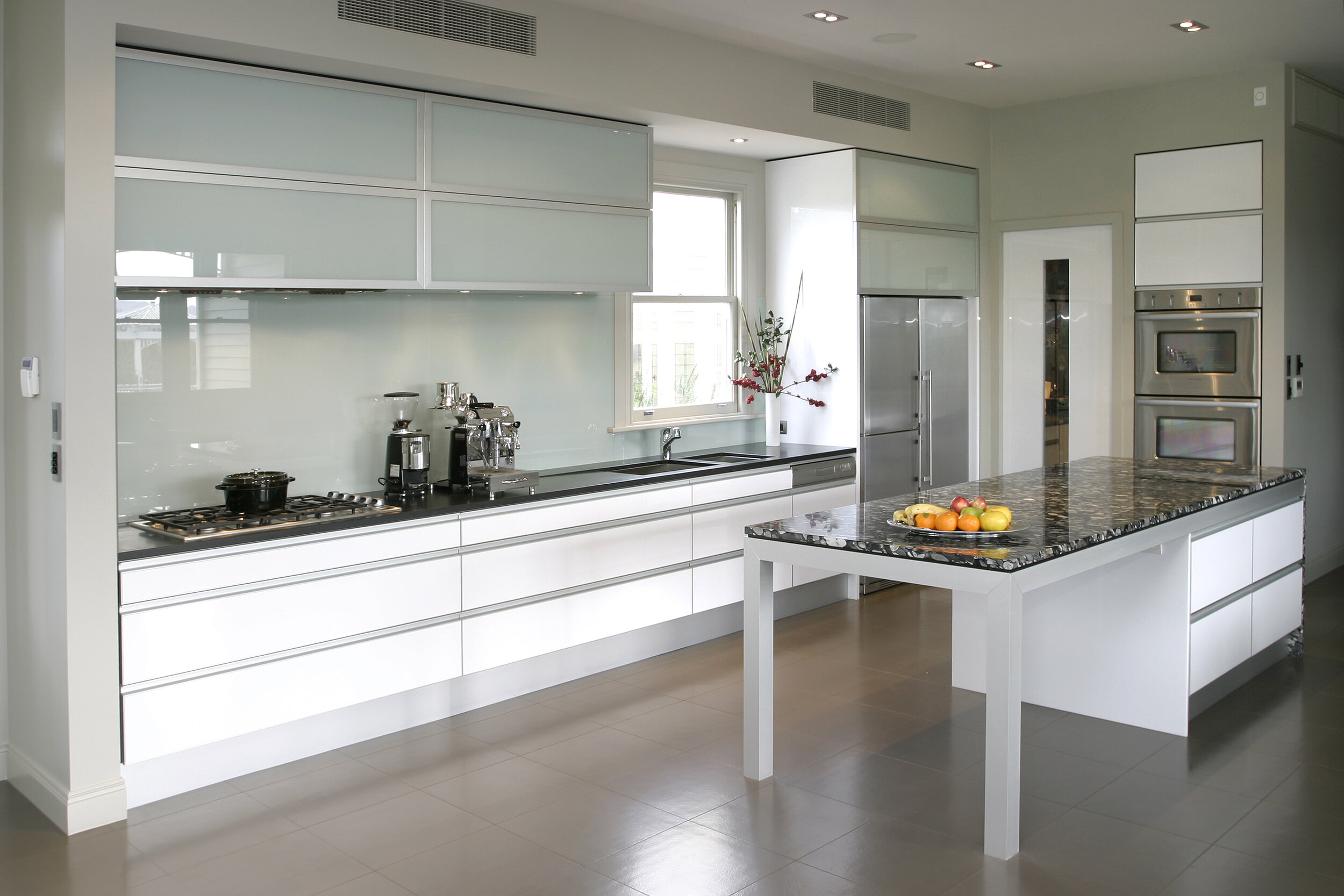 Contemporary white kitchen with palette of gloss white cabinetry, aluminium framed detailing, coloured glass and natural stone