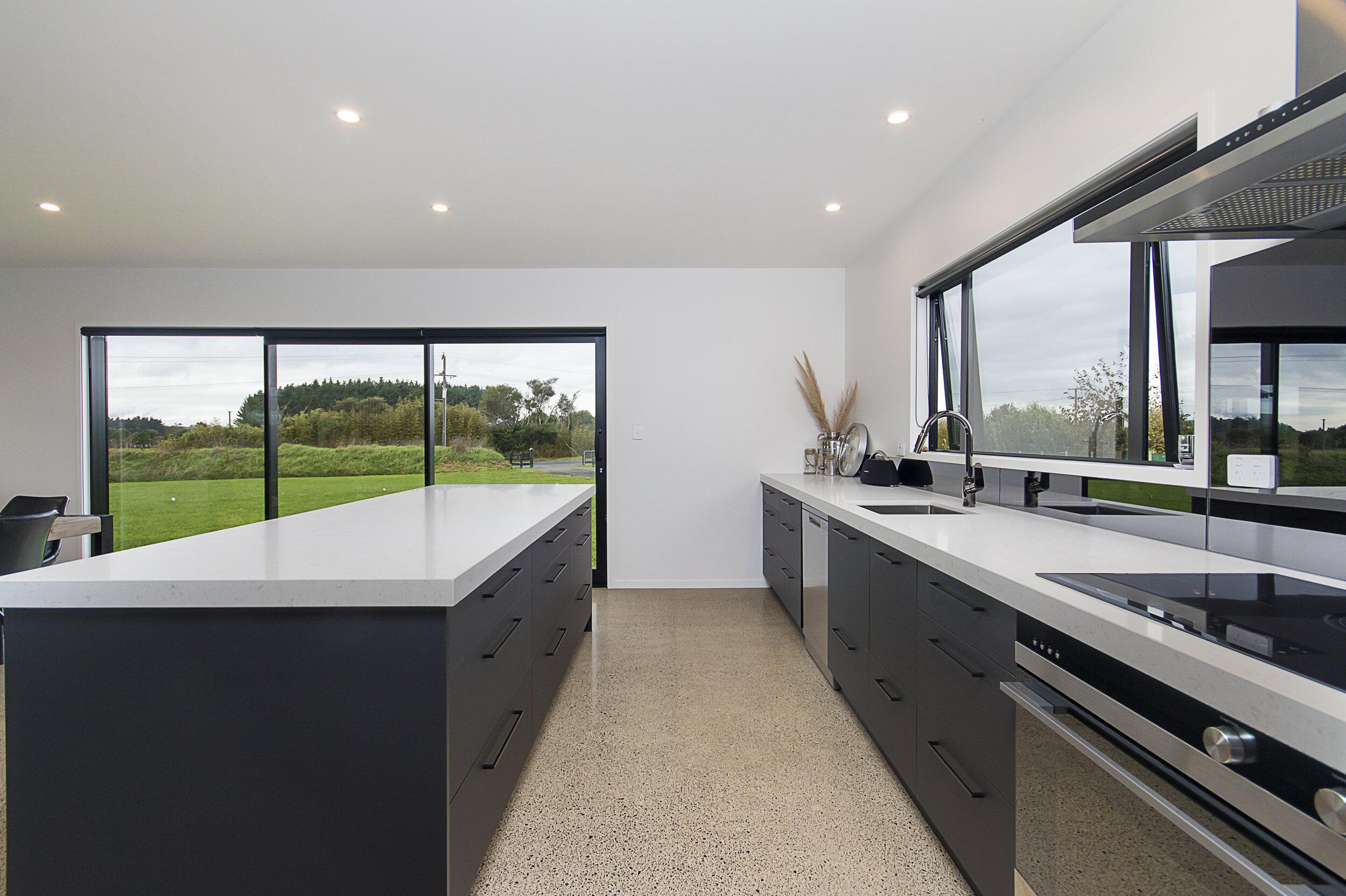 Grey mirror splashback in modern kitchen with dark cabinetry and white benchtop