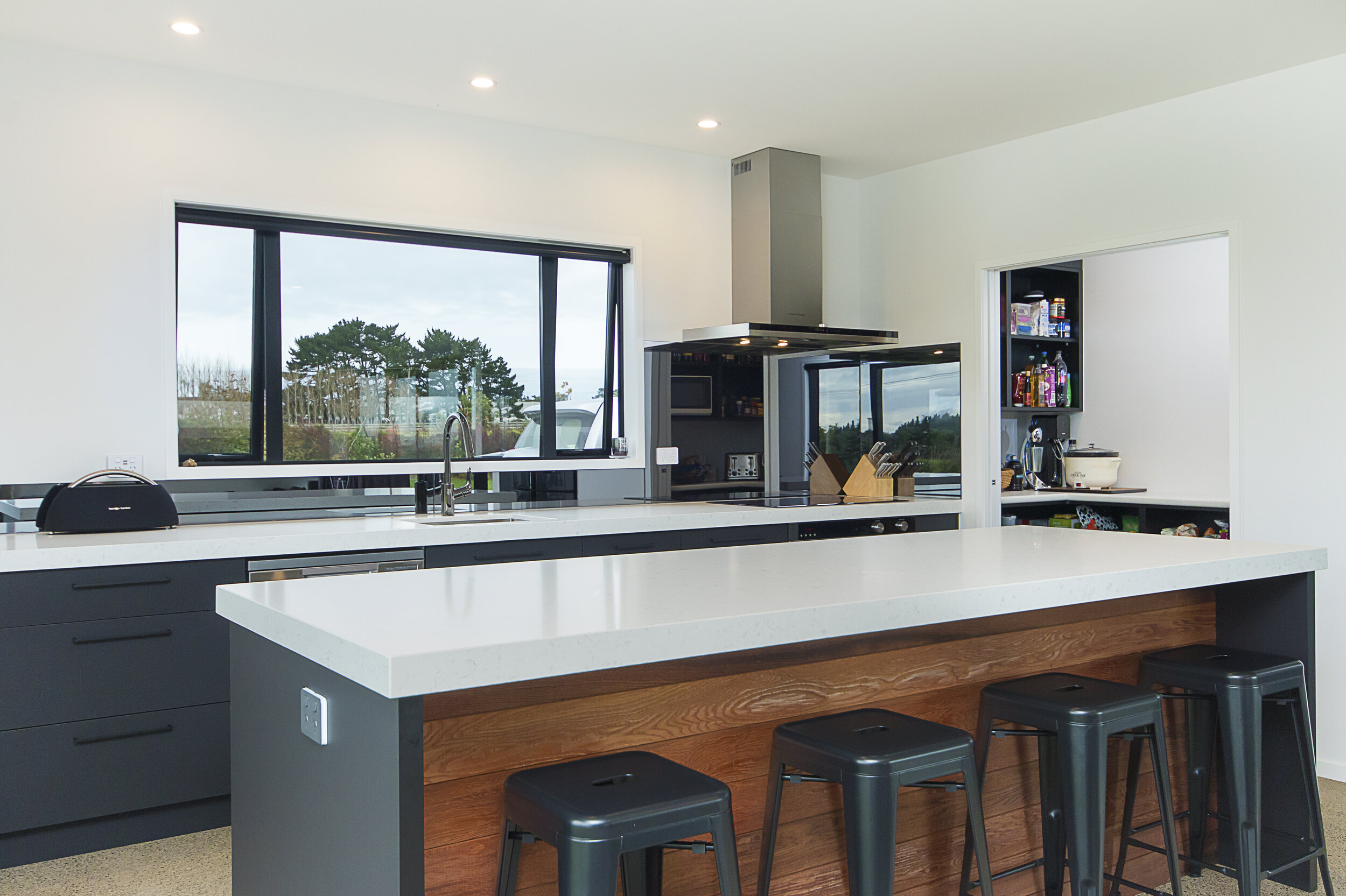 Mirrored grey glass splashback in modern kitchen with white benchtop and grey cabinetry