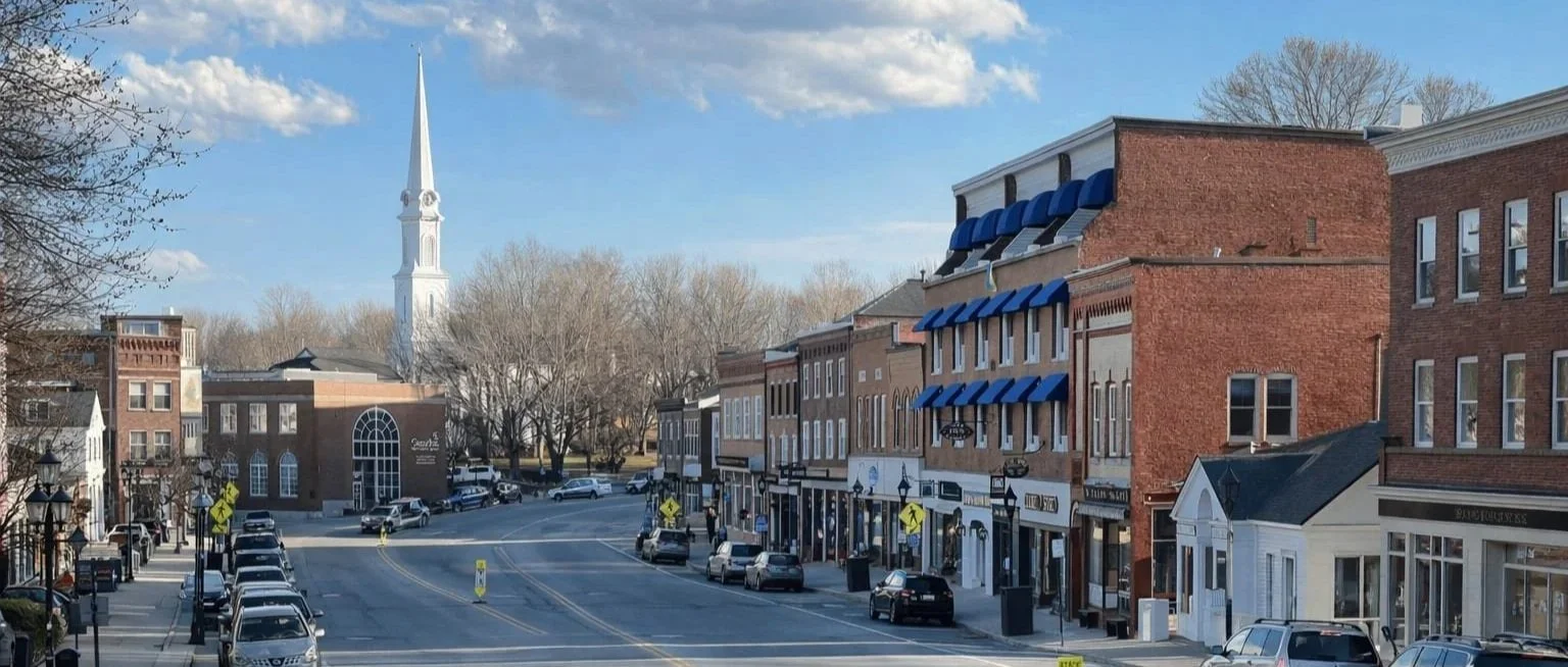 Downtown Camden Maine with shops, parked cars, and church steeple along Main Street