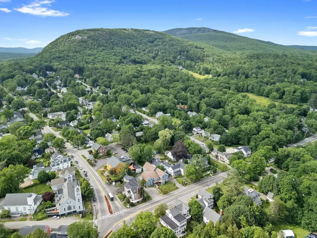 Aerial view of a small town surrounded by dense green trees and rolling hills.