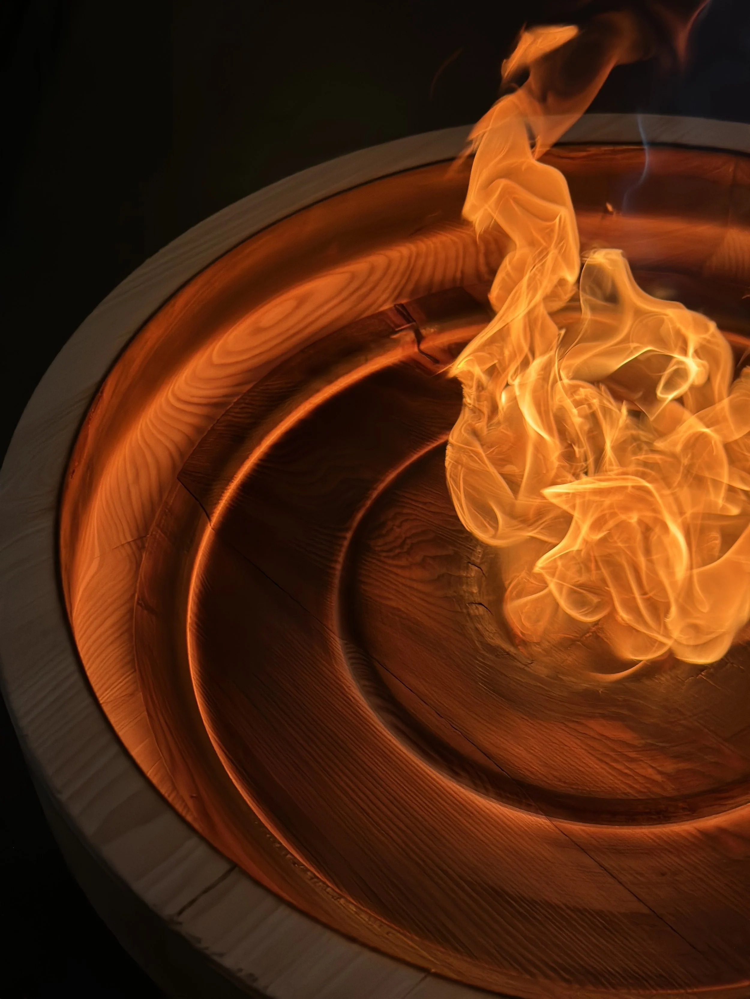 Close-up of a wood fire burning inside a round, light-colored wooden container with visible grain.