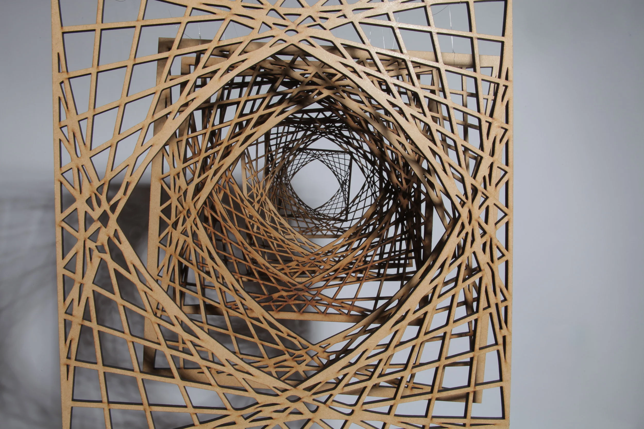  This piece is based on a mathematical geometry sequence, which has been translated into a physical form.  The laser-cut sculpture was suspended and extends into space. Lights were used to cast projections, animating the work and creating a complex p