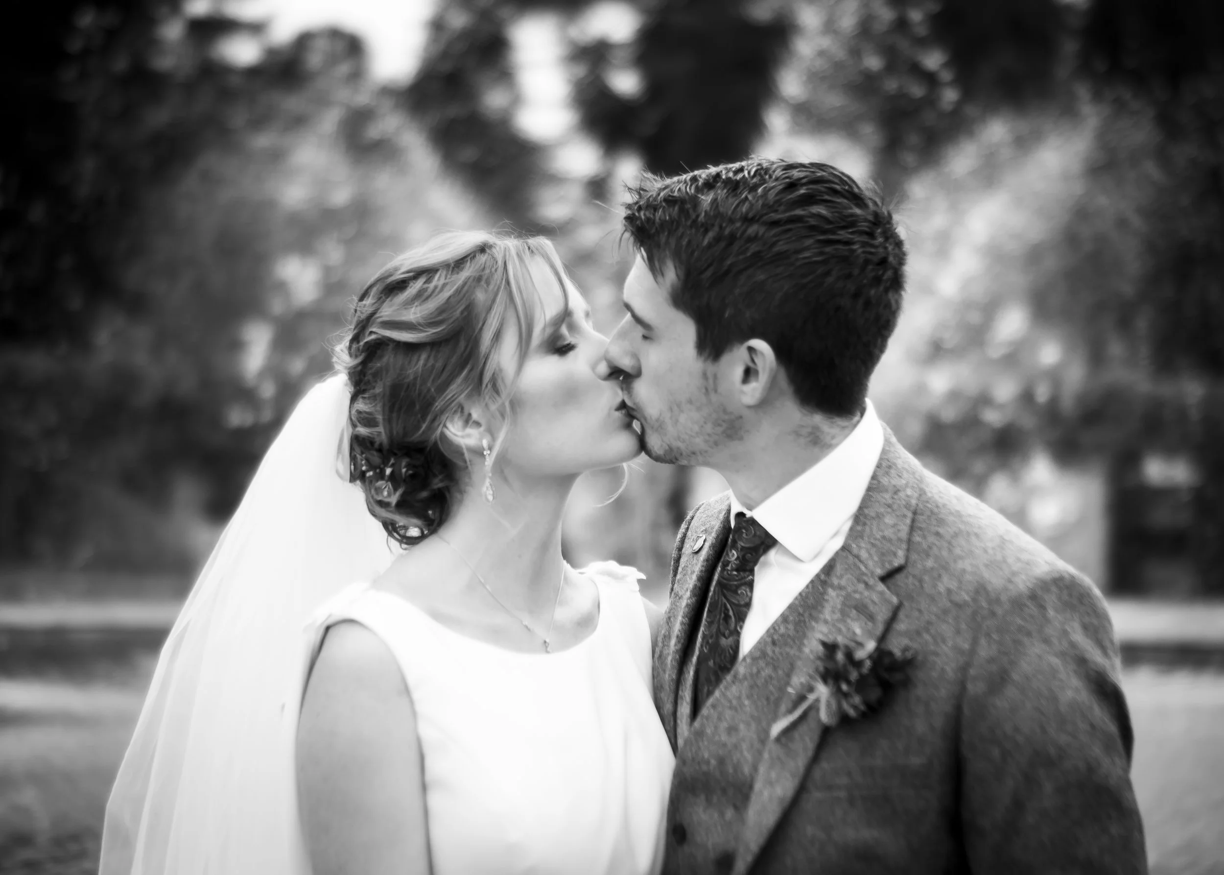 Bride and groom kissing on their wedding day in a black and white film photograph.