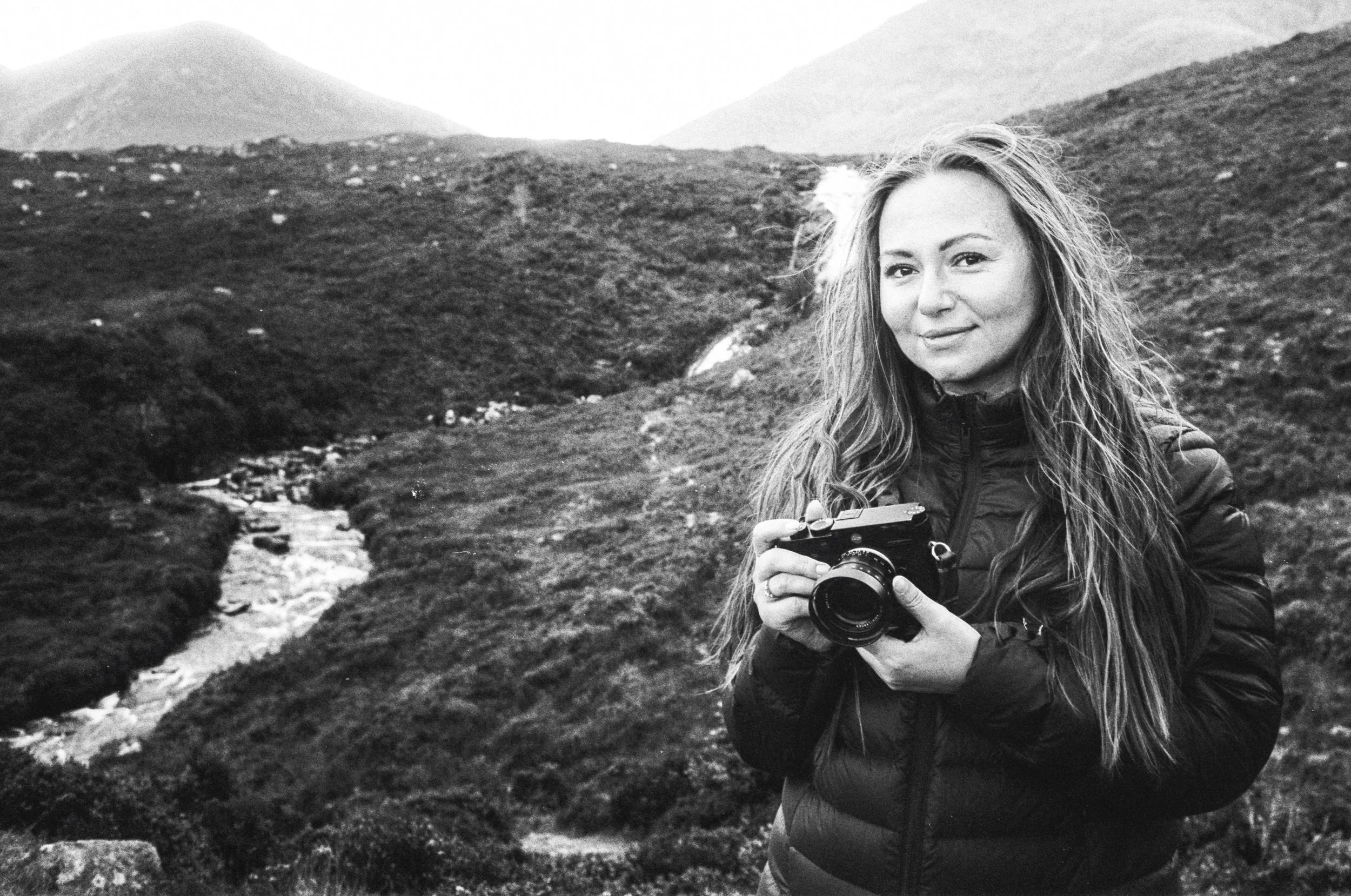 Black and white 35mm photograph of a photographer holding a camera in an open landscape, used to illustrate next-generation film scanning for photographers across the UK.