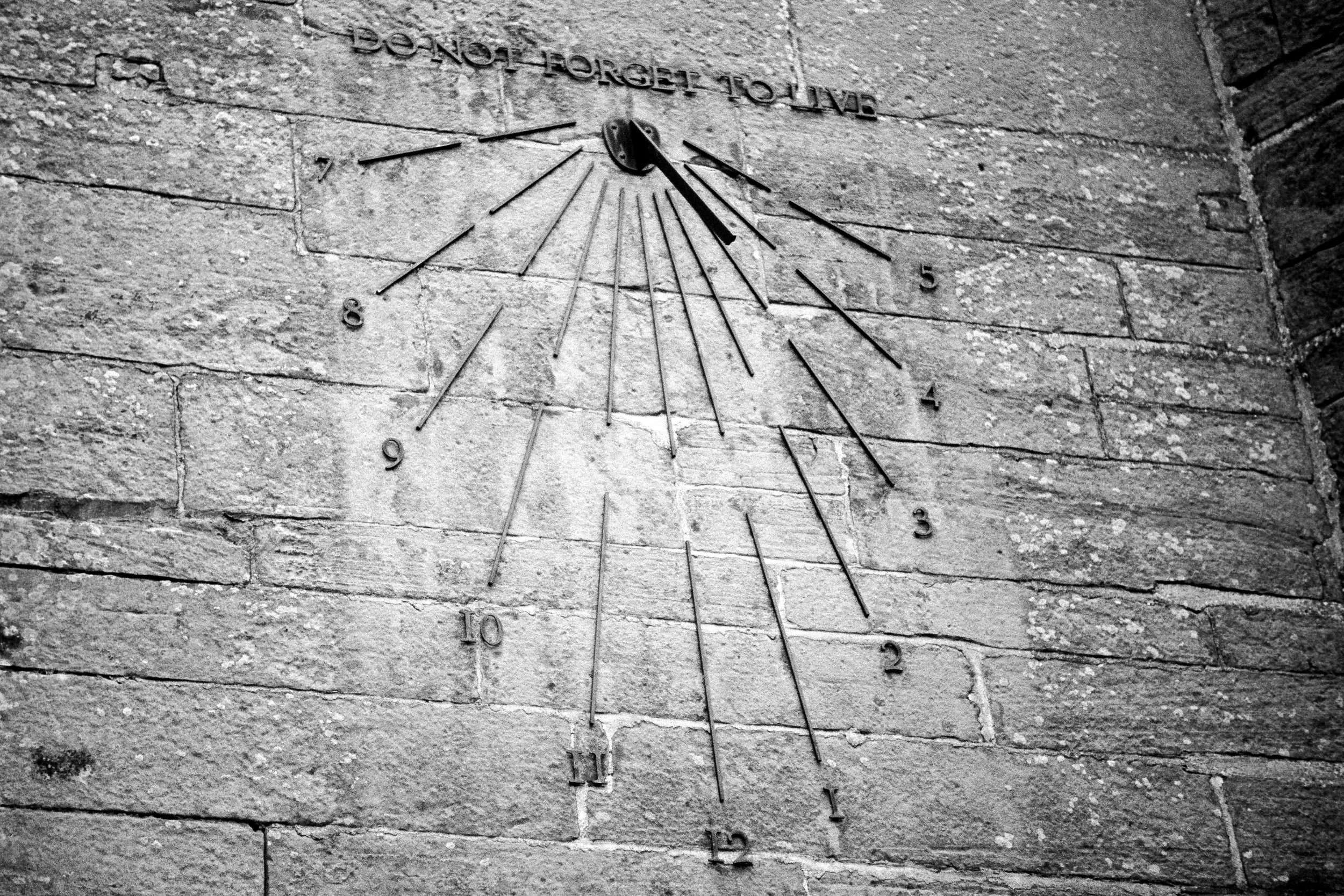 Black and white photograph of a stone sundial wall with the words “Do not forget to live”, developed from AHU VISION3 film and scanned at Liquid Light Lab