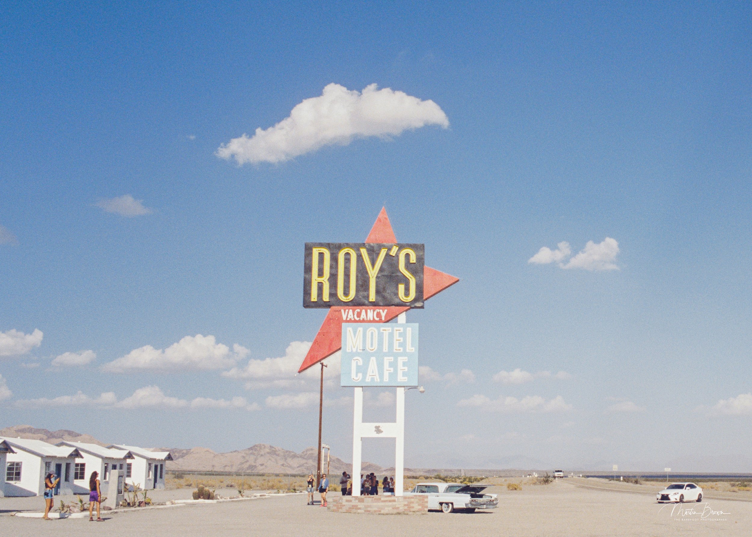 Colour negative film scan showing a roadside motel sign beneath a blue sky, demonstrating the colour and file quality produced by Liquid Light Lab film processing and scanning.