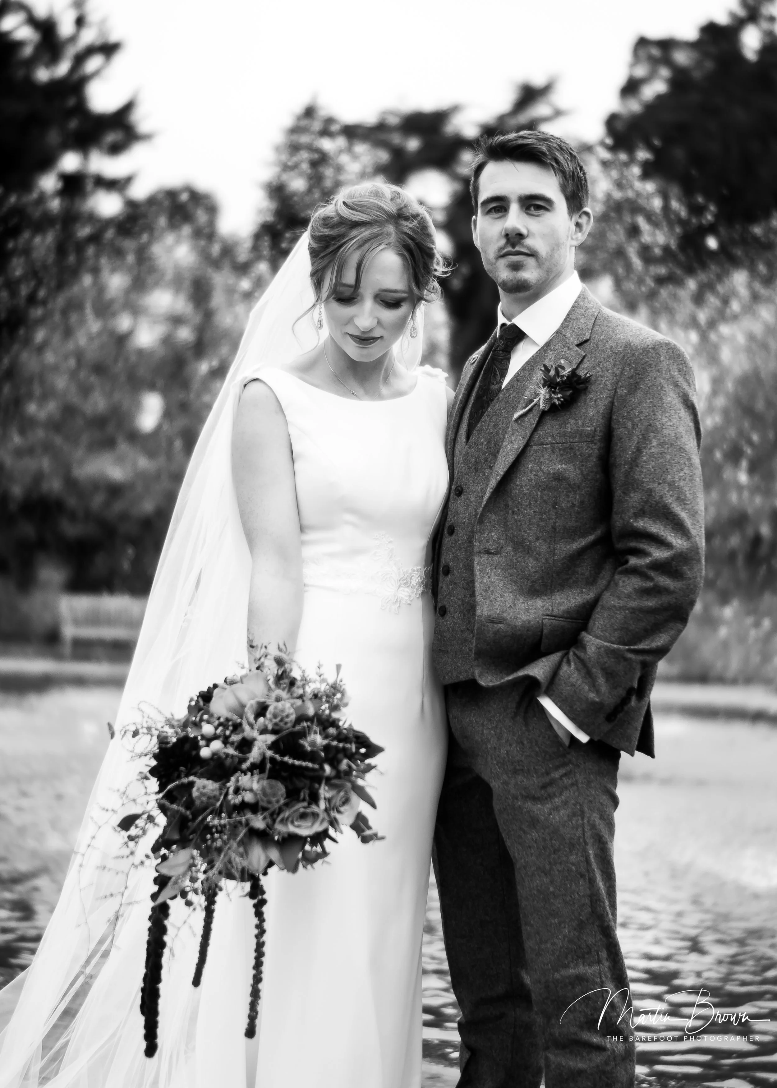Bride and groom standing together outdoors in a black and white wedding portrait photographed on real film.