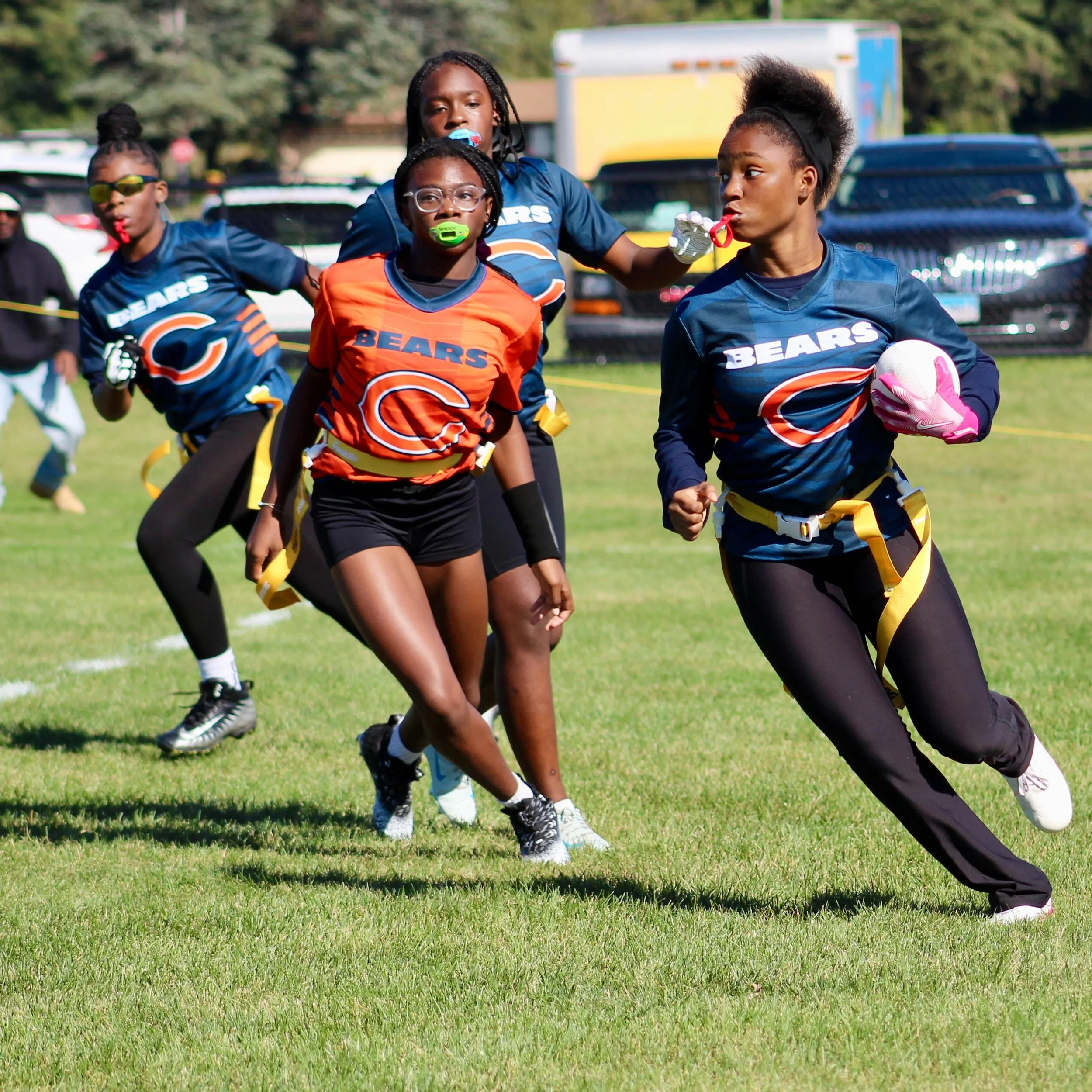 Young child wearing a red hockey jersey, helmet, and skates, playing hockey on an ice rink, preparing to hit a puck with a hockey stick.
