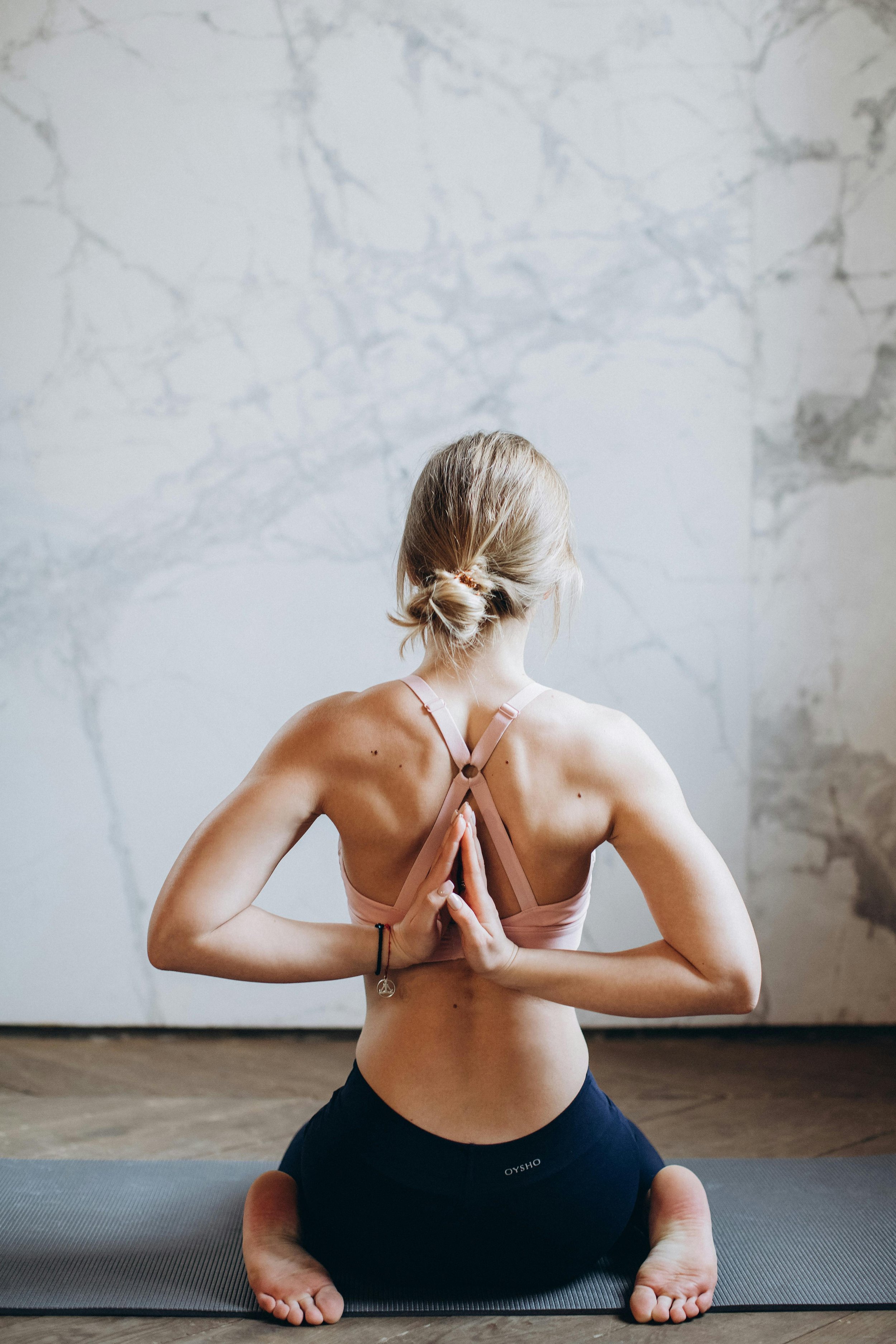 White woman in a yoga pose, torso turned to reveal a defined and muscular upper back, emphasizing strength and spinal alignment. Natural lighting highlights the muscle contours and posture precision.