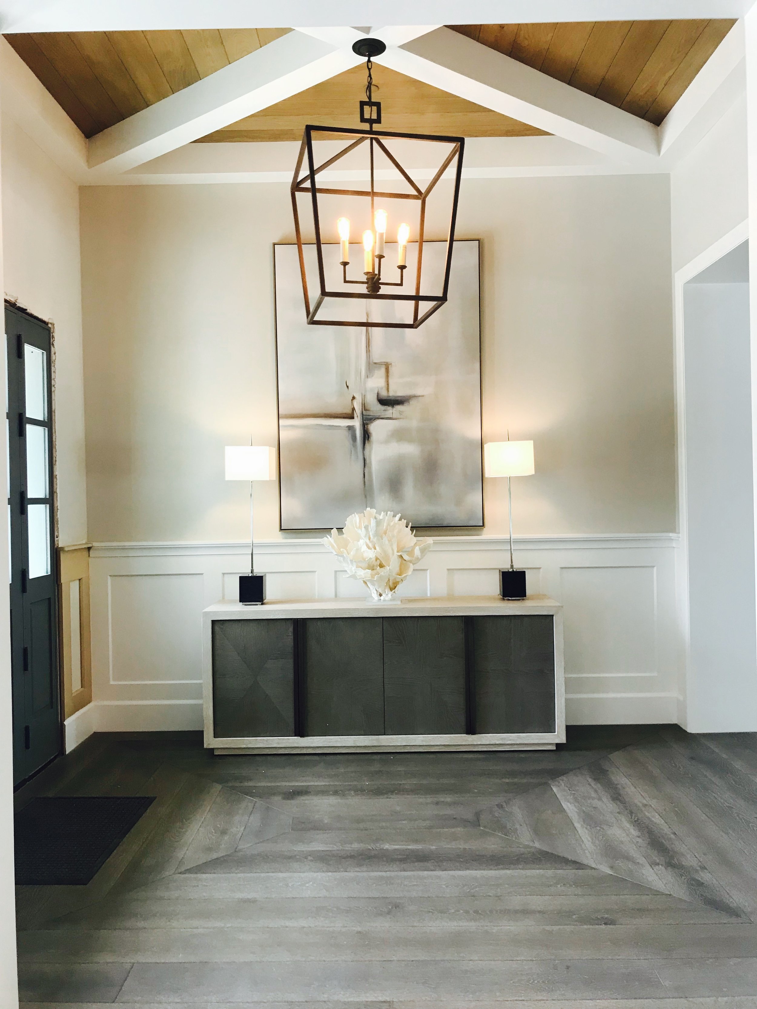 A central dark iron chandelier suspends from cross beams at the ceiling with warm wood T&G between.