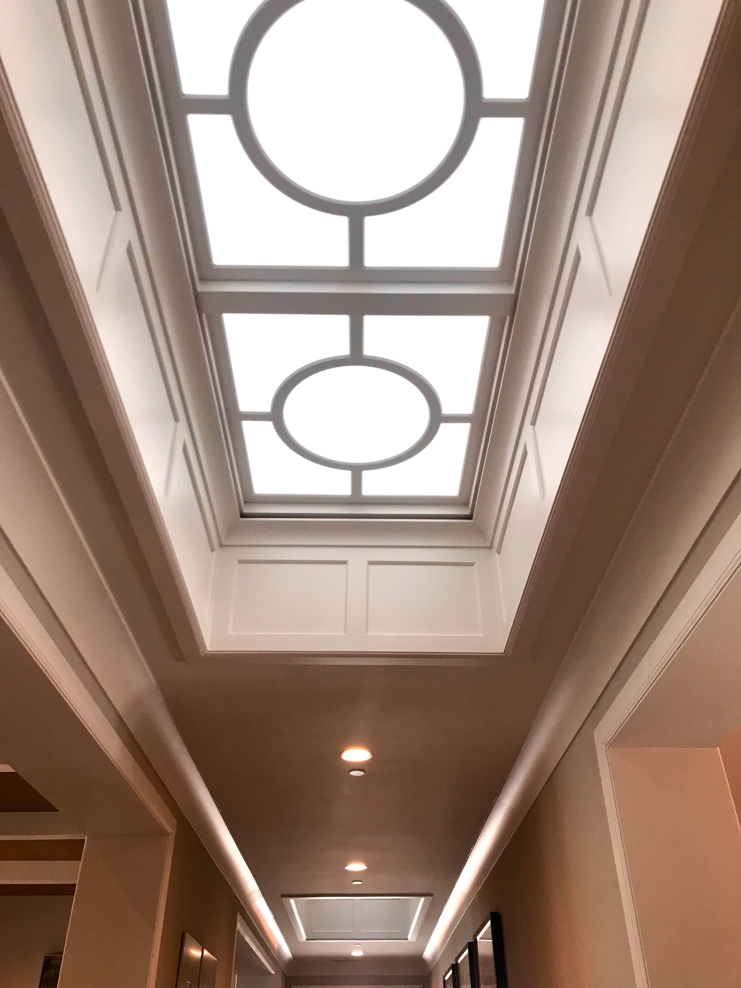 Custom skylights allow natural light along the main path of travel, paneling surrounds the sides of the ceiling alcove with circular moulding and frosted acrylic insets above.