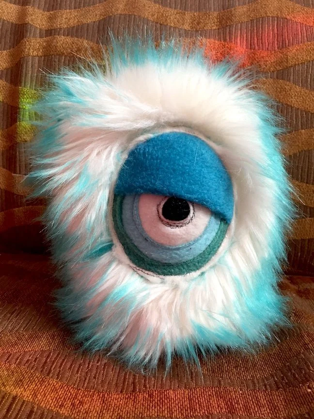 SMALL SNOW MONSTER WITH ONE SLEEPY EYE WITH BLUE ACCENTS