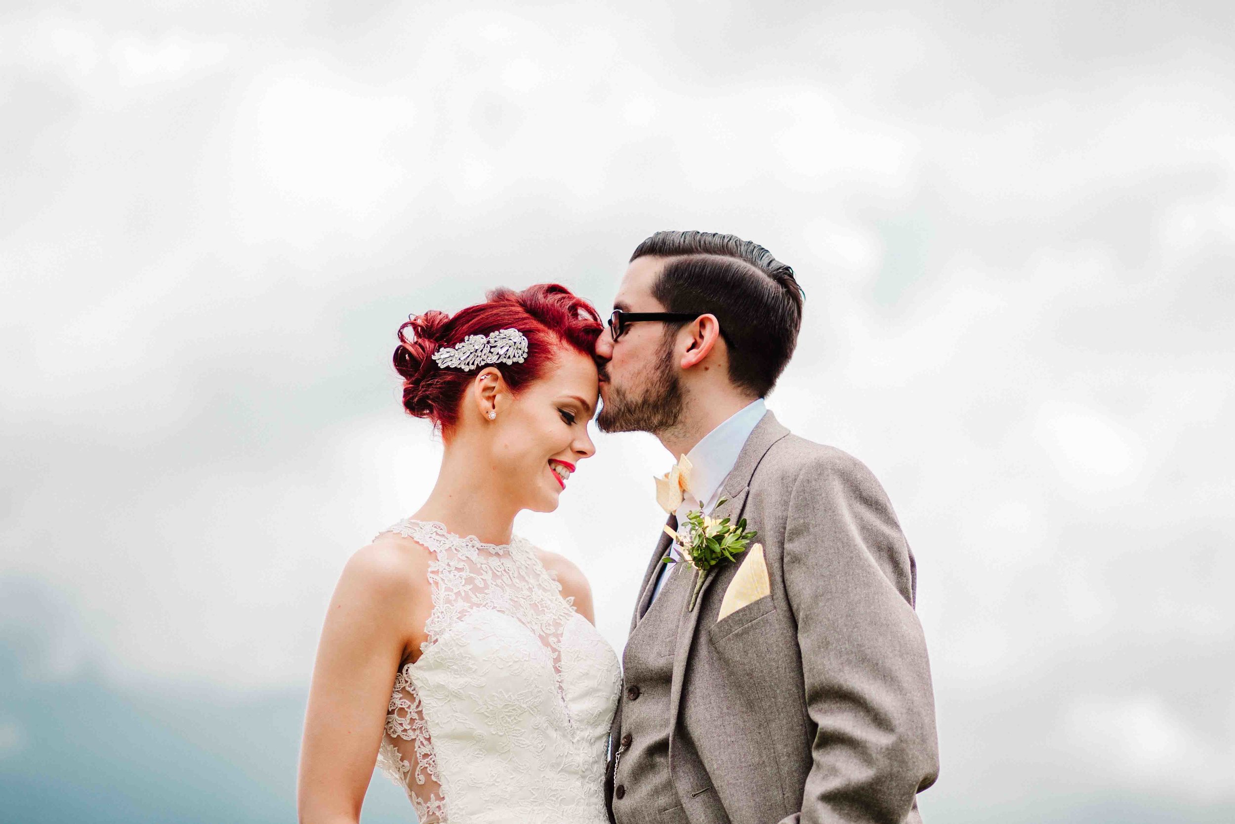 A groom kissing his bride on the forehead