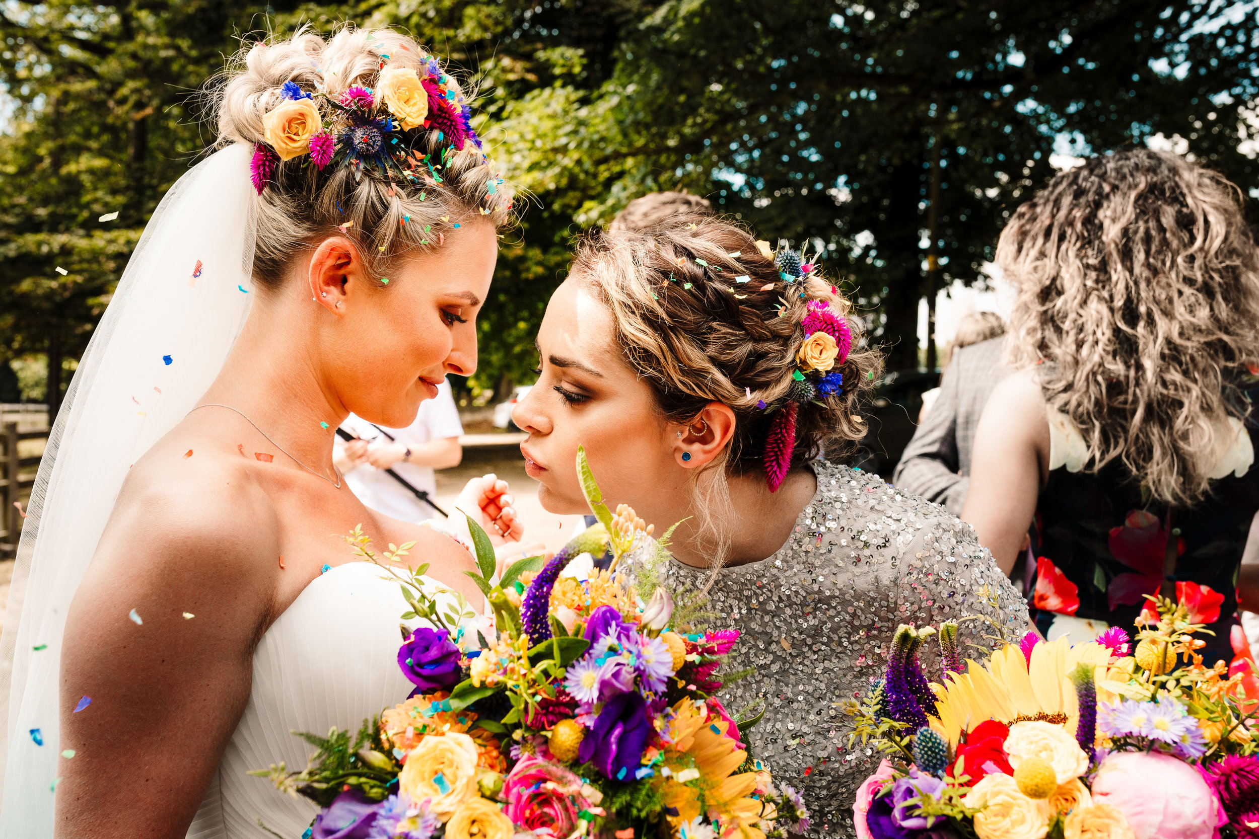 A bridesmaid blowing confetti off a bride's chest