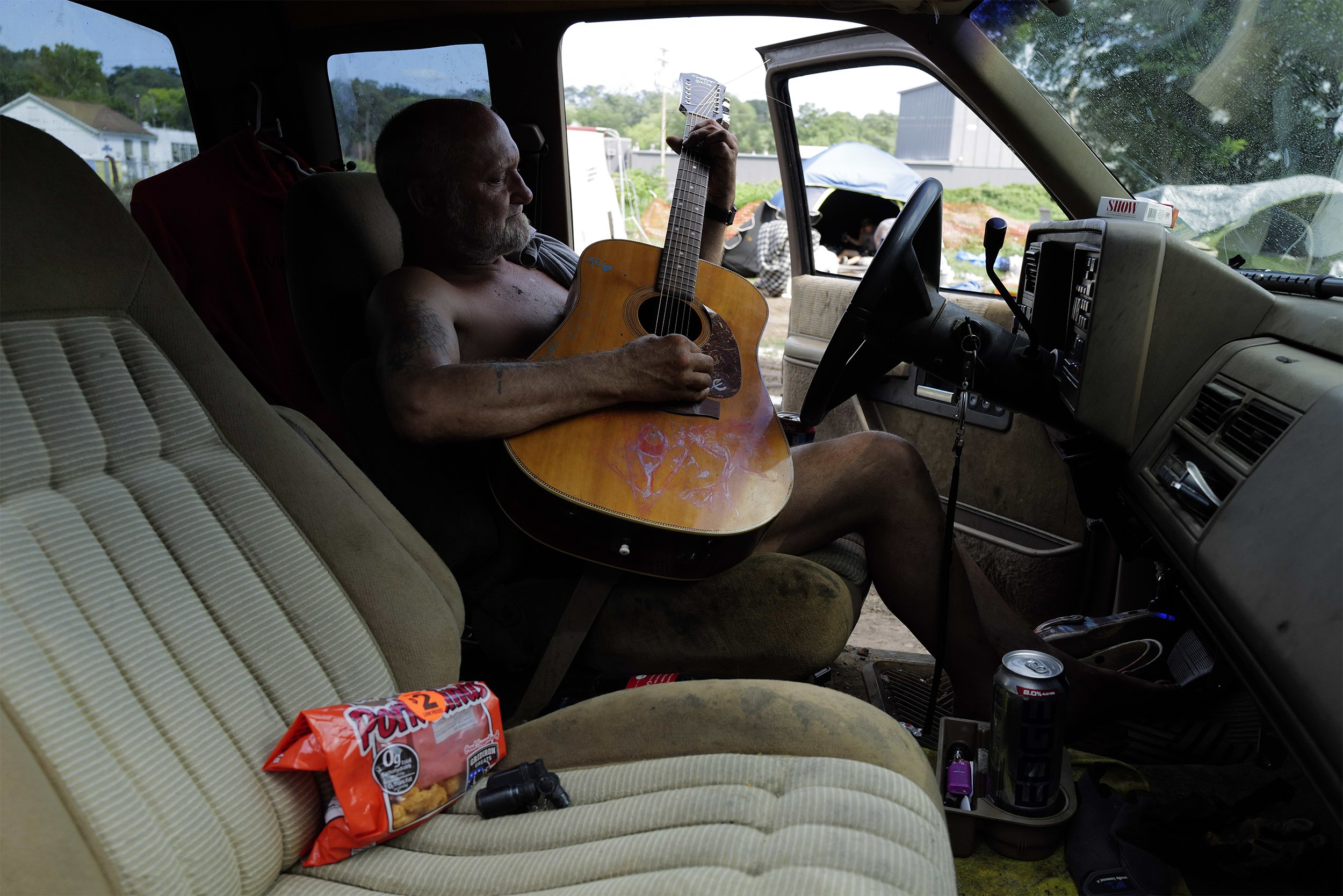  Michael Stanfill, 61, plays guitar in his car at the Ampersee Avenue homeless encampment in Kalamazoo on Wednesday, August 25, 2021. Residents were ultimately evicted from the encampment in the months of September and October with the city having no