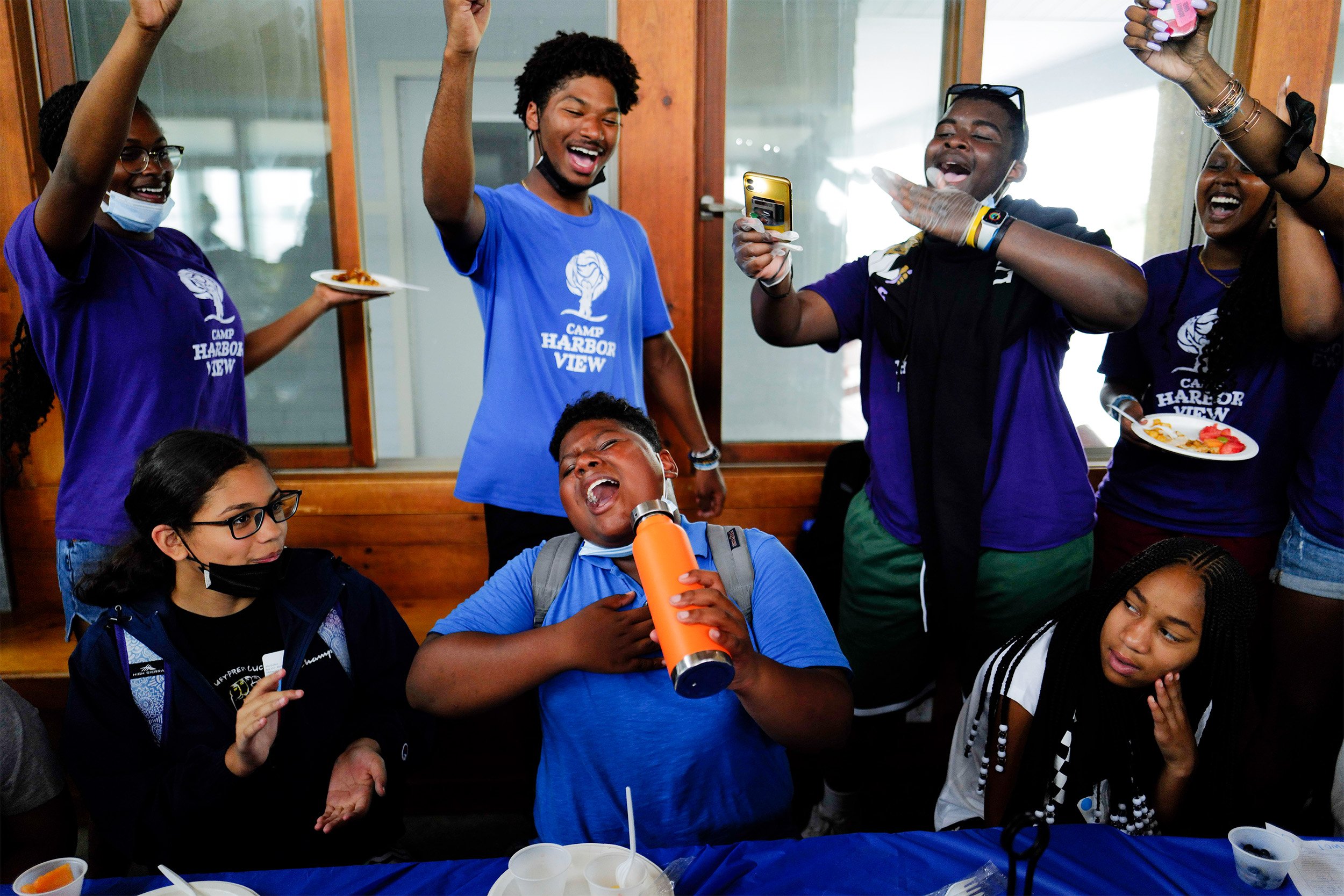  Devin Hernandez (center) sings along to “Super Bass” by Nicki Minaj during lunchtime with counselors at Camp Harborview on Long Island, Mass., on July 18, 2022. Meal time is filled with upbeat music tracks, games and chanting.  