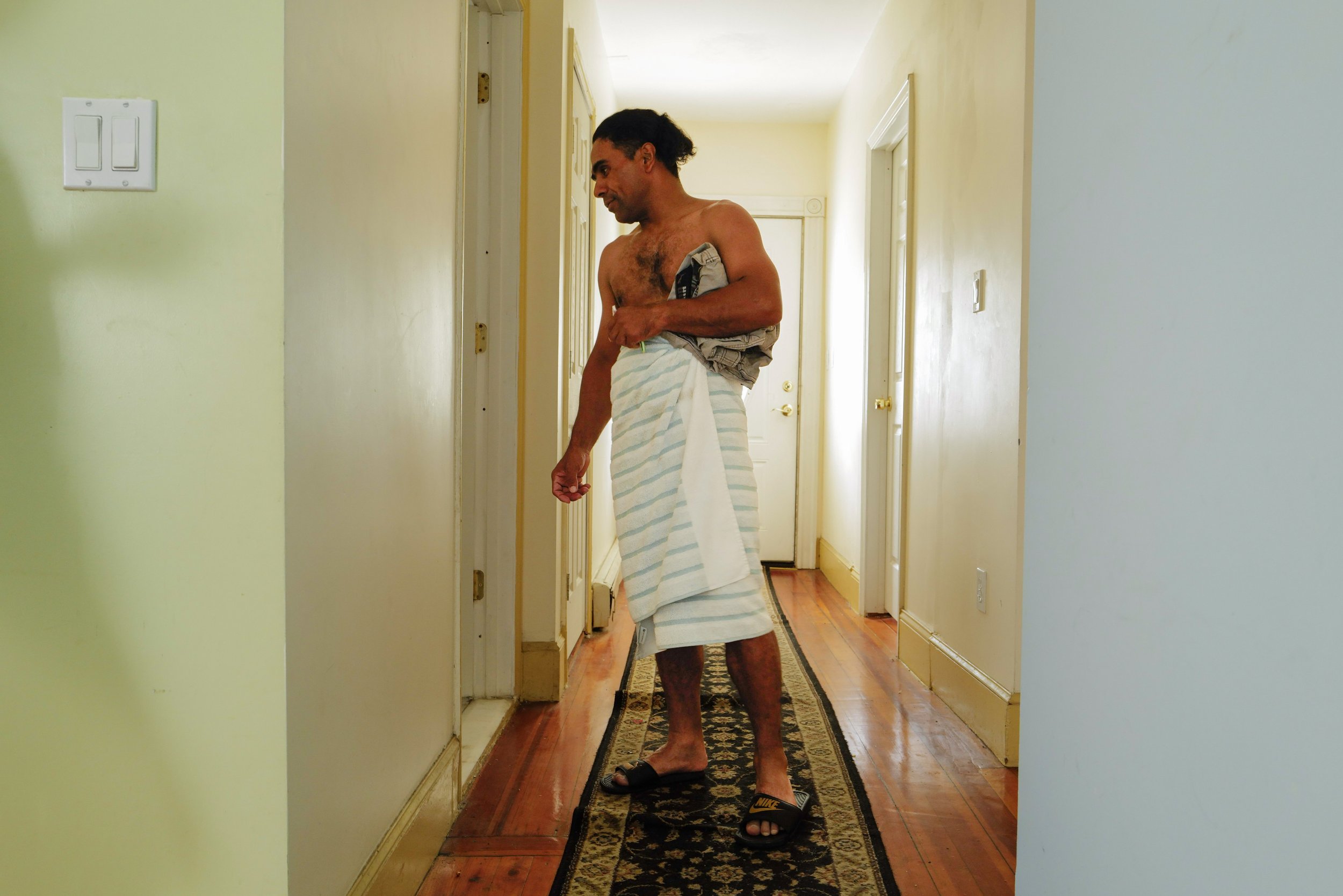  Manuel waits to use the shower shared with 12 tenants while getting ready to head to one of his two jobs at the old residence in Somerville, Mass. on August 31, 2022. 