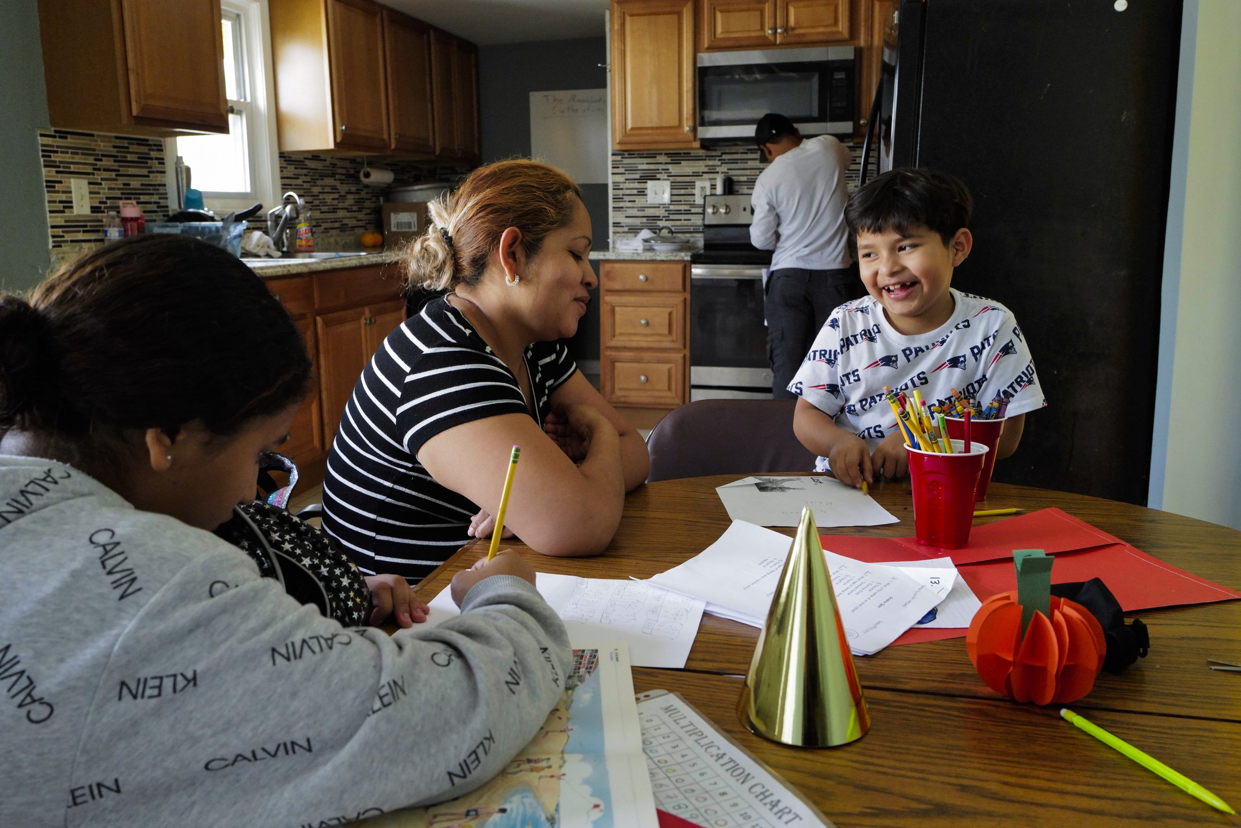  (From left) Manuel’s daughter Fernanda Aimee, 12, Teresa and her son Raul Alexis, 6, work on schoolwork together while Manuel cooks rice and beans in the kitchen of their new apartment in Somerville, Mass. on Sept. 30, 2022.  
