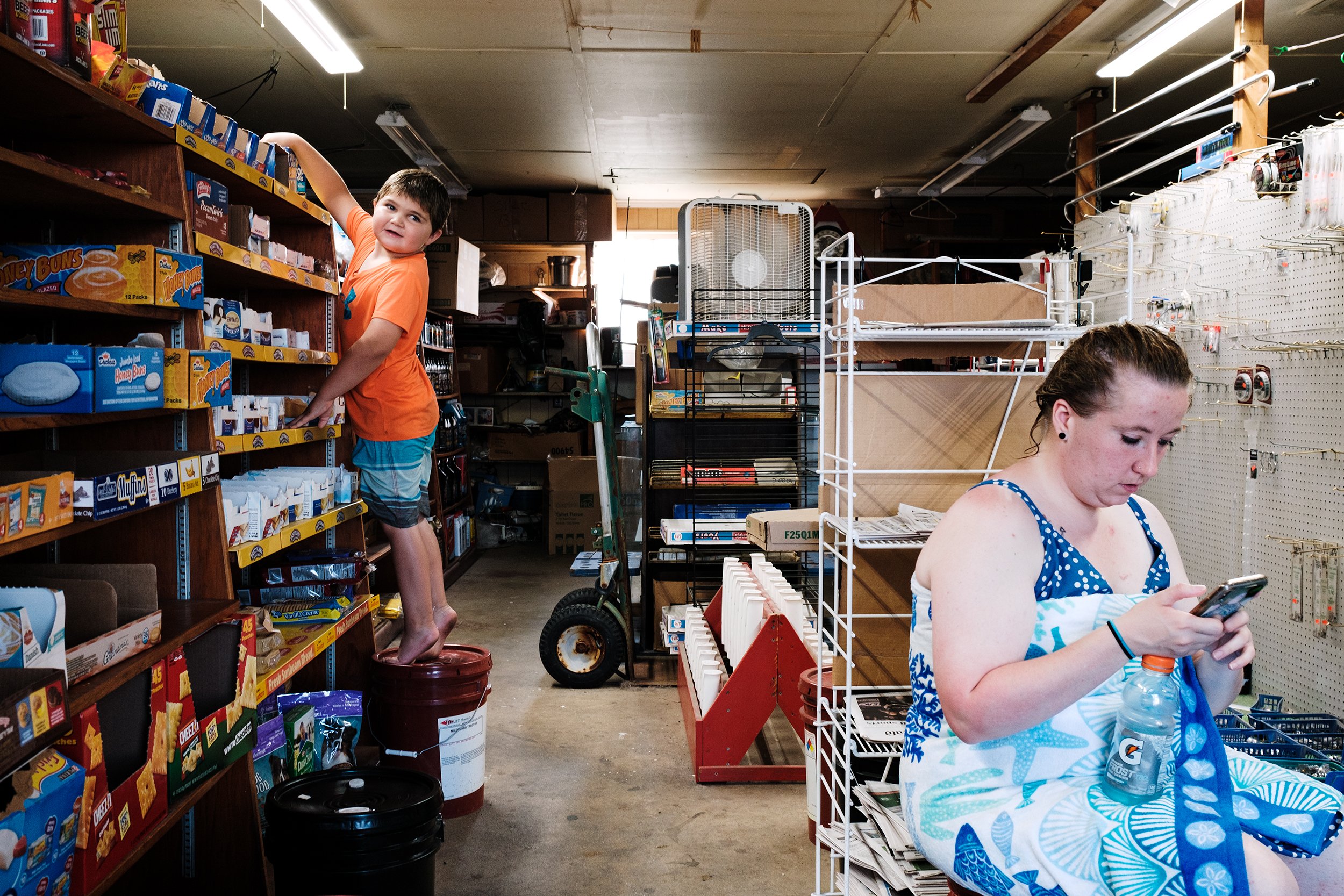  Luke Holloway, 6, reaches for Pop-Tarts at Arby’s General Store in Deal lsland, while Kelsie Holland checks her phone. The bait and tackle rack has been empty since Covid-19, due to a lack of tourism.  
