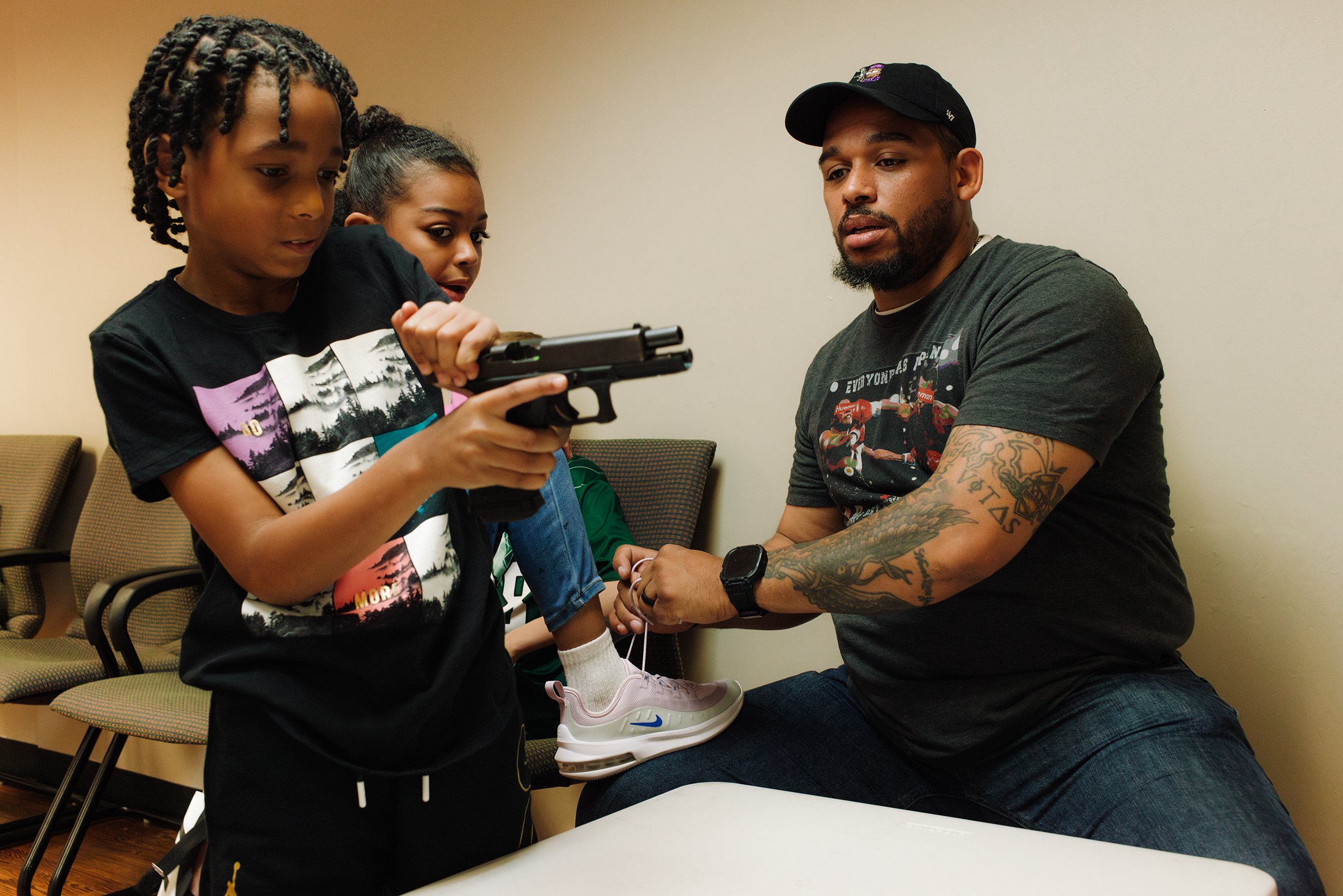  Donkor Minors ties his daughter, N.A. Minors’, 10, shoe while instructing David Vazquez-Parker, 10, how to properly load and unload a handgun at The Don Firearms training in Mattapan Square in Boston.  As of October, there have been 530 mass shootin