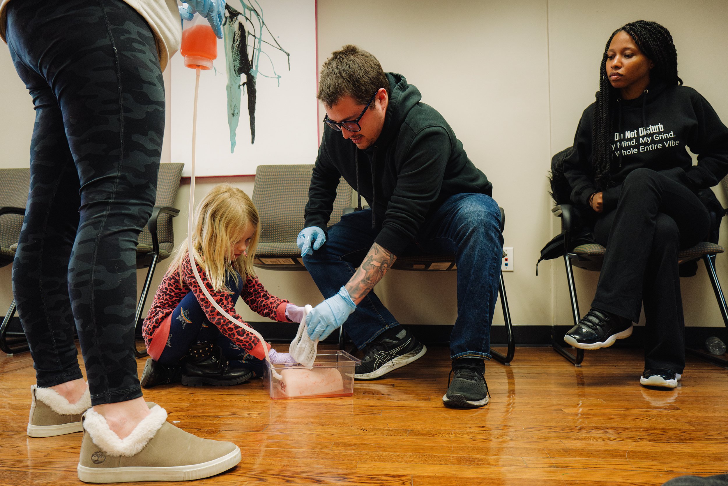  Vivian McAllister, 6, with the help of Tim LeBrasseur, practice packing a wound in the event an artery is severed from a gunshot. Water that is dyed red is used to simulate bleeding from the fake artery and is then plugged with gauze containing a he