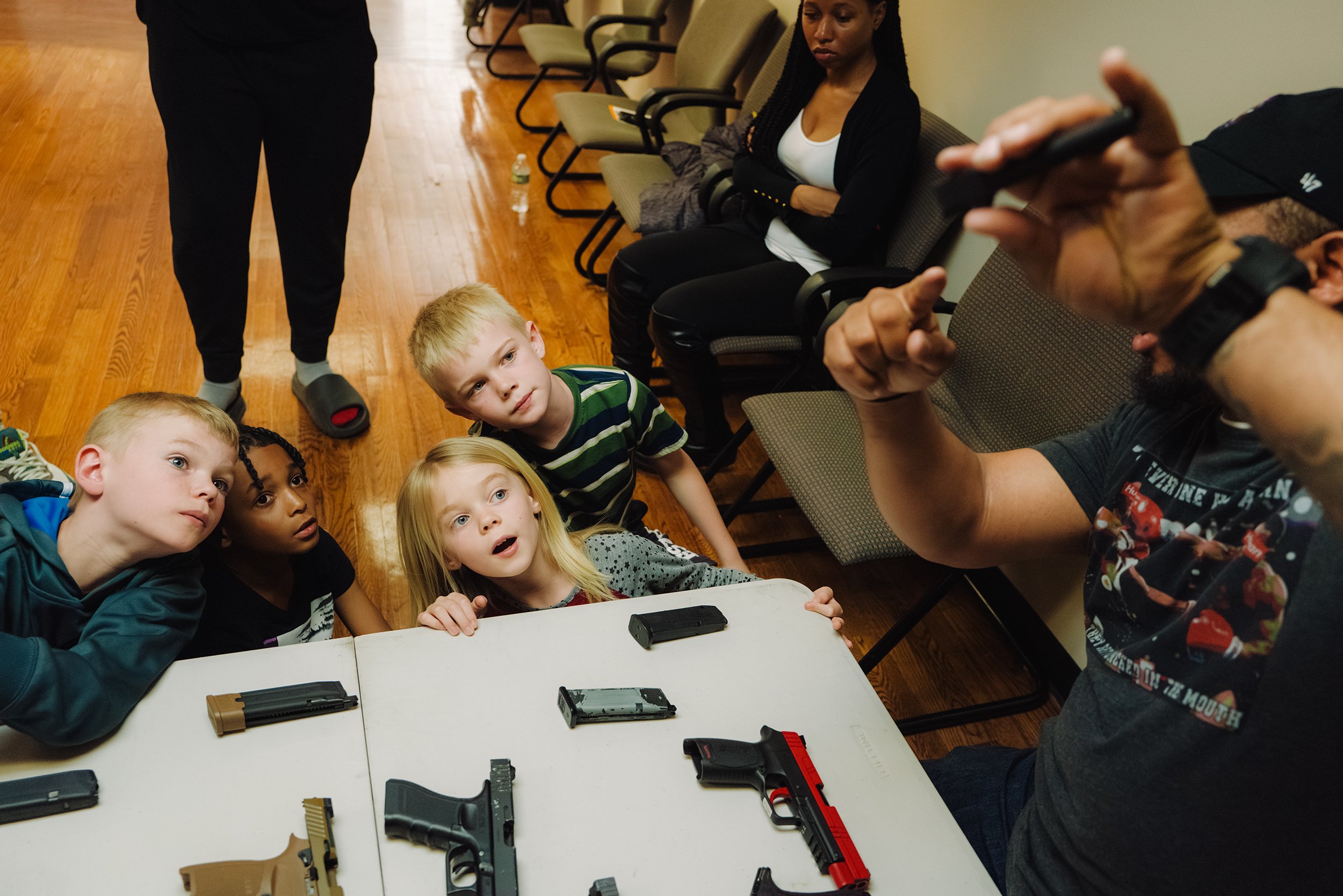  (From left) Jack McAllister, 8, David Vazquez-Parker, 9, Vivian McAllister, 6, and Ben McAllister, 10, look up at Donkor Minors demonstrating how to properly load and unload a magazine into a handgun. During the lesson, kids work with both airsoft a