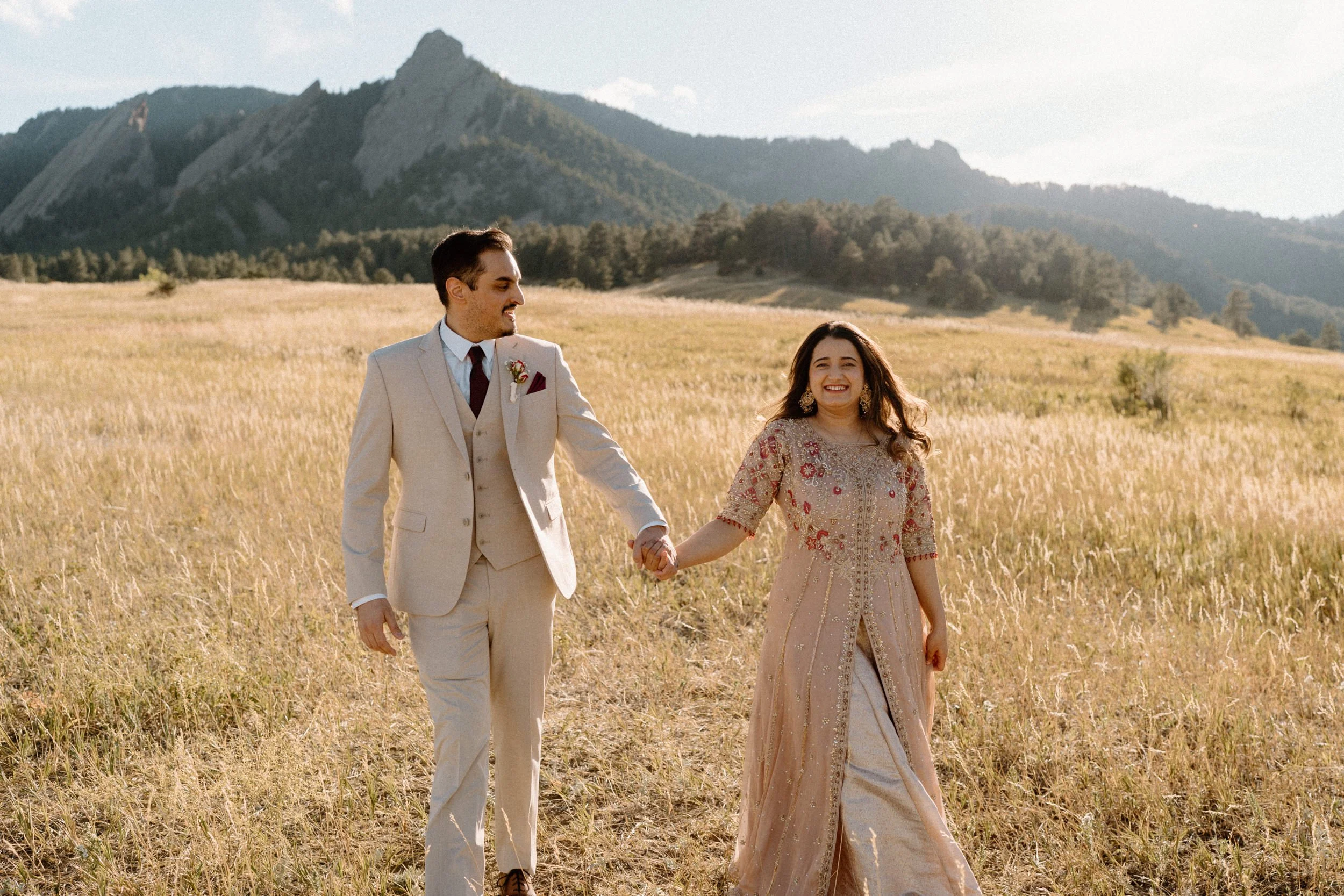 Couple holding hands and hiking in a field during an engagement session in Boulder Colorado