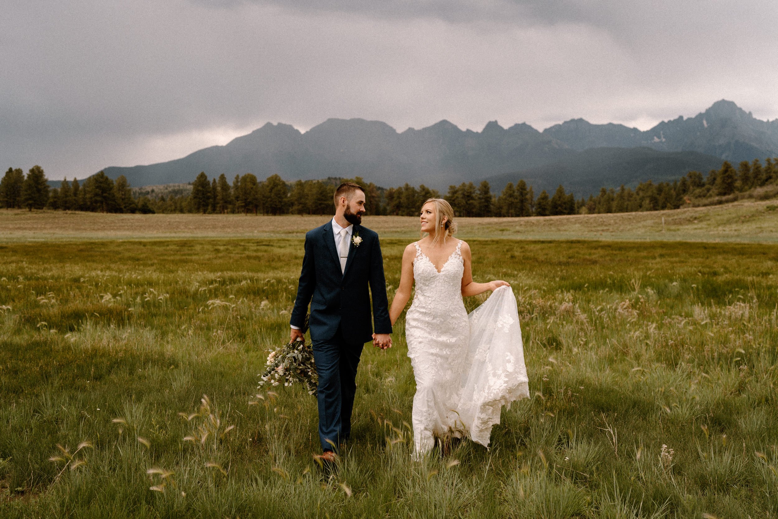 Bride and groom hold hands as they walk through a valley at Top of the Pines in Ridgway, CO