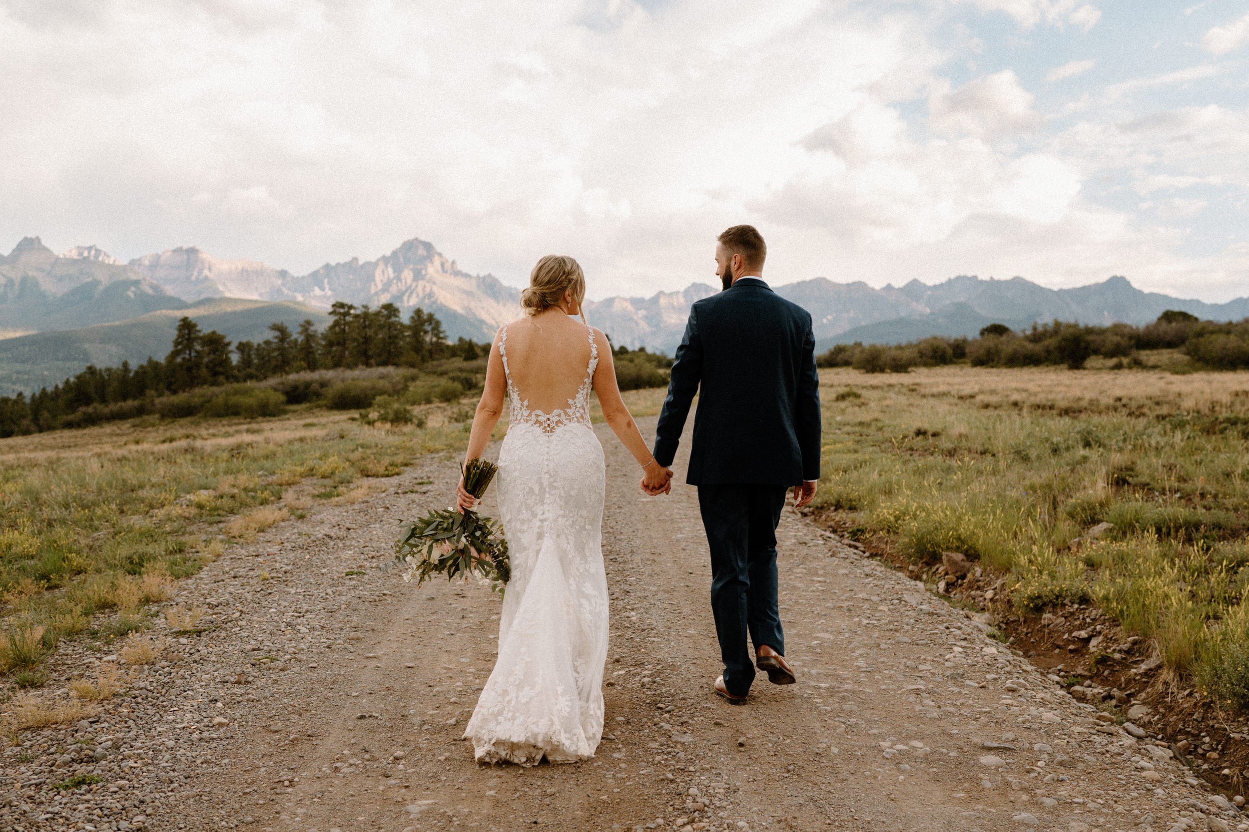 Bride and groom walk down dirt road at Top of the Pines in Ridgway, CO