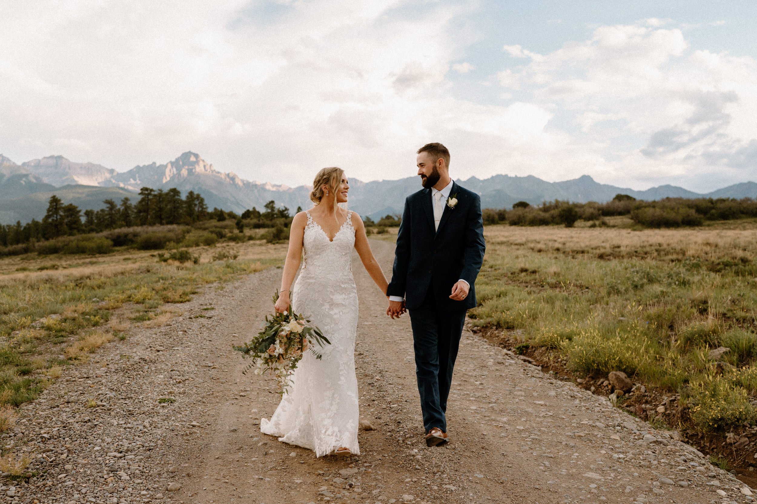 Bride and groom smile as they walk down the dirt road together at Top of the Pines in Ridgway, CO