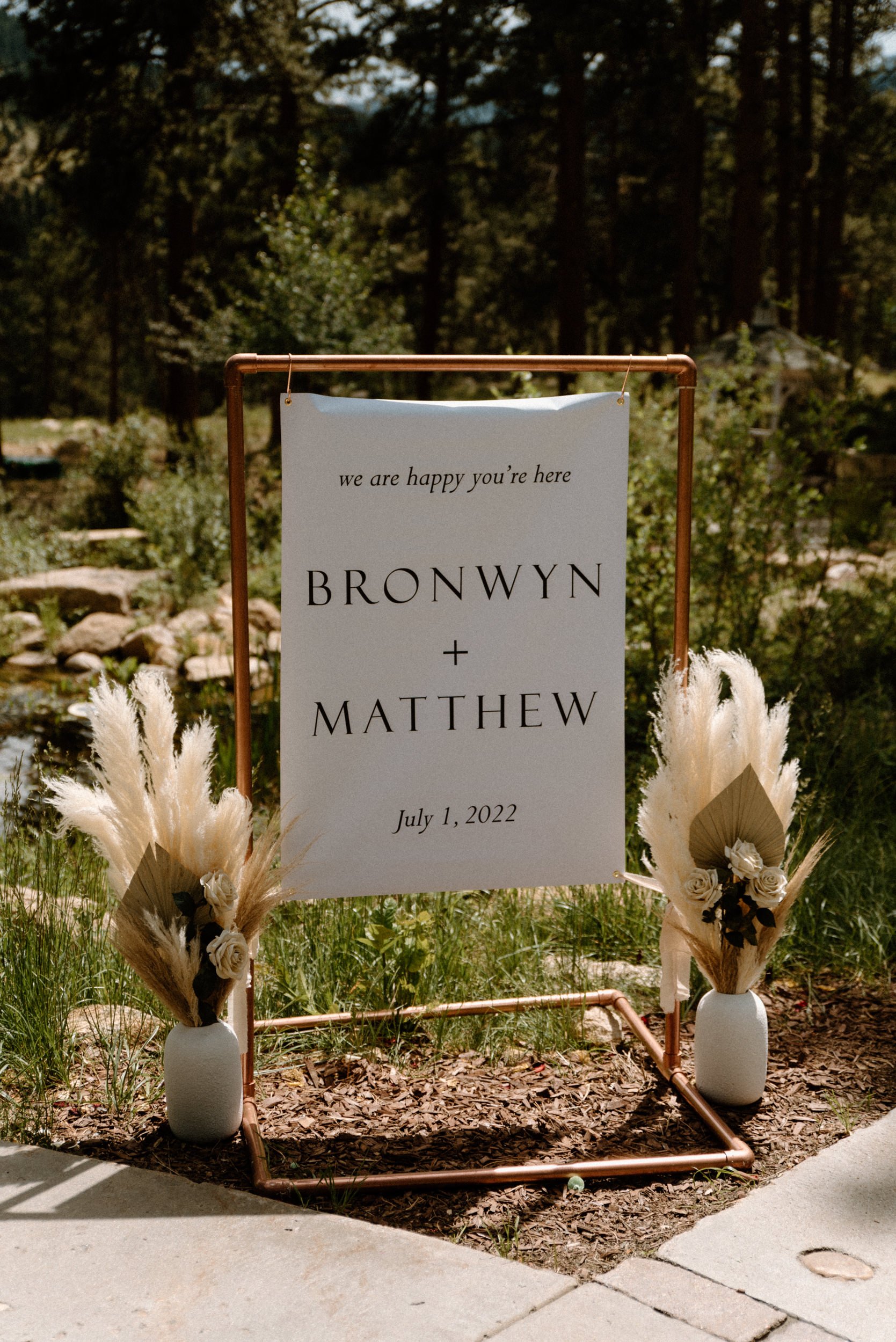 A white sign reads "We are happy you're here. Bronwyn + Matthew. July 1, 2022"