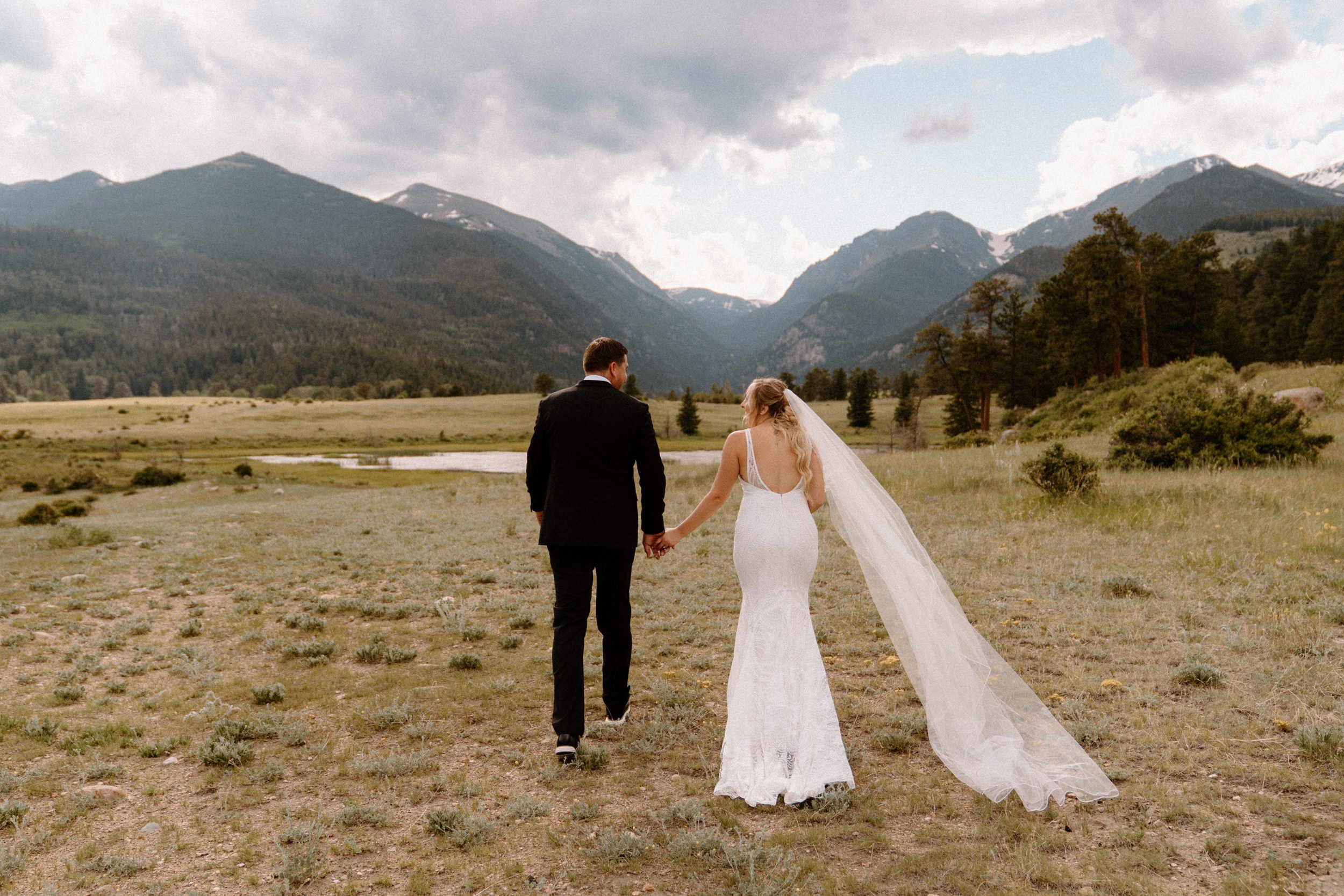 The bride and groom hold hands as they walk through a mountain valley in Estes Park, CO