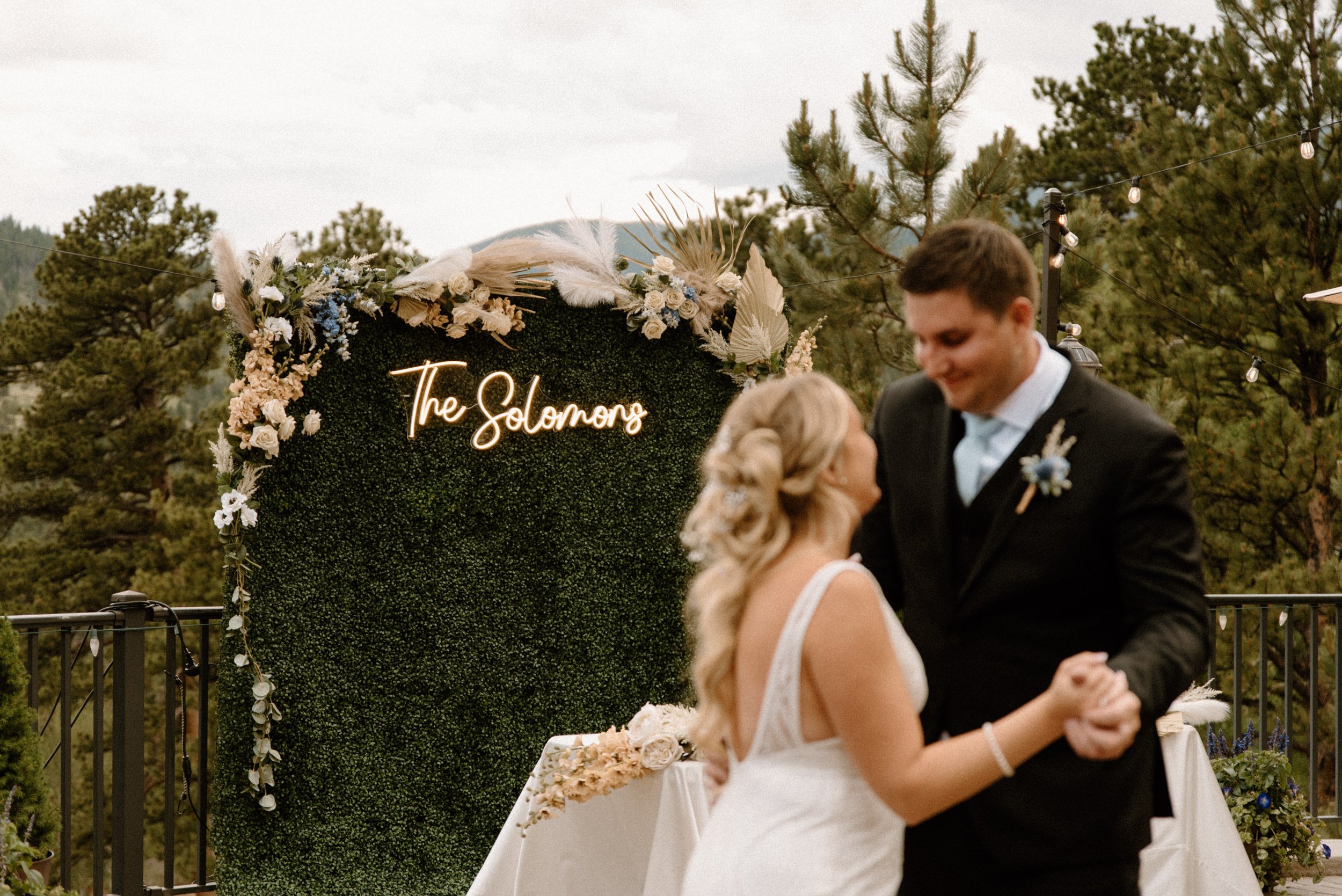 The bride and groom share their first dance as a neon sign that reads "The Solomons" shines in the background