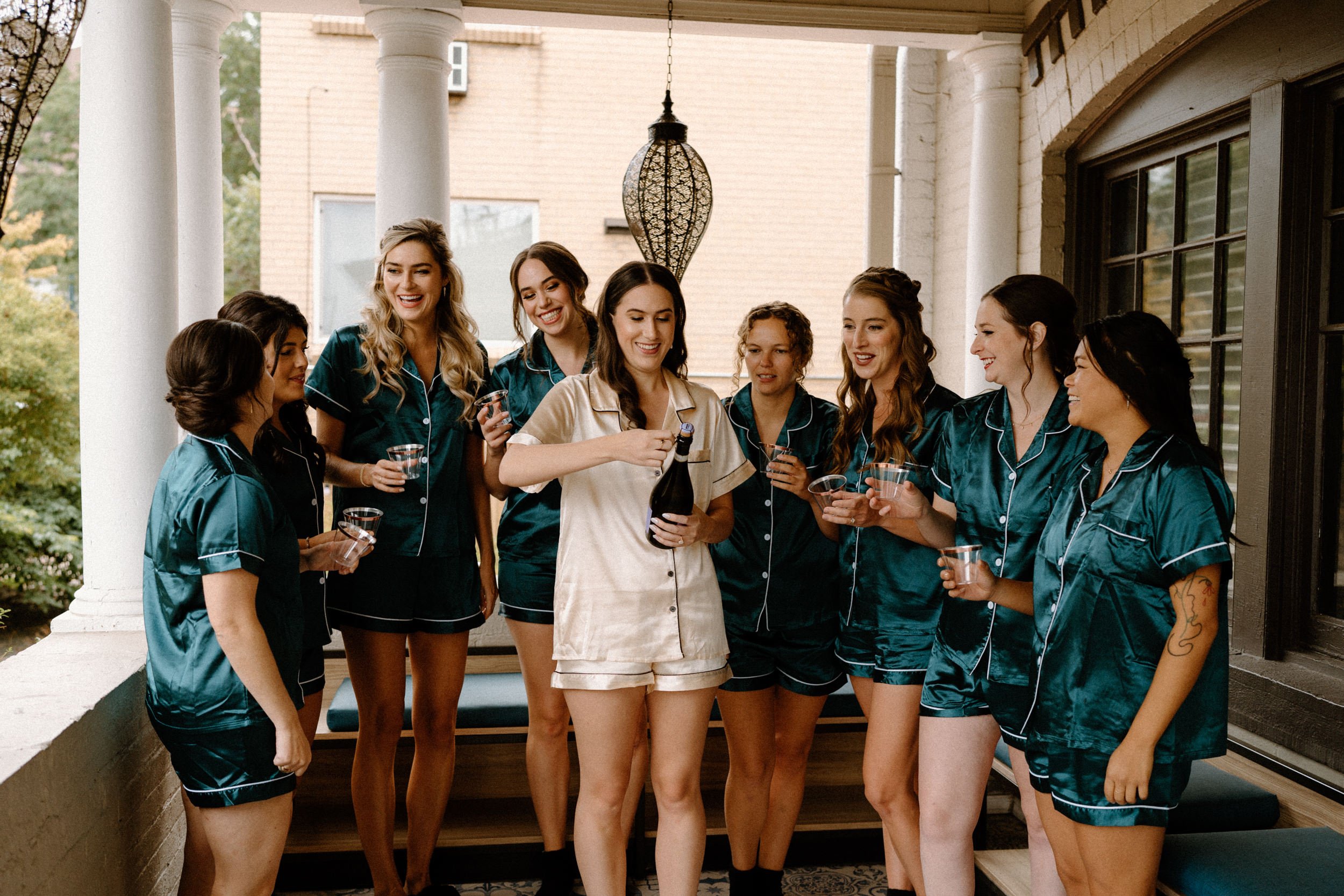 The bride opens a bottle of champagne with her bridesmaids while getting ready