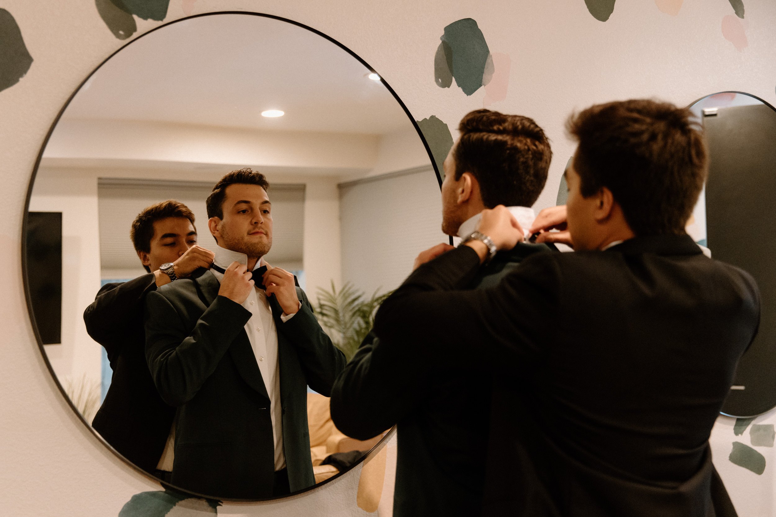 A groomsmen helps the groom with his bowtie