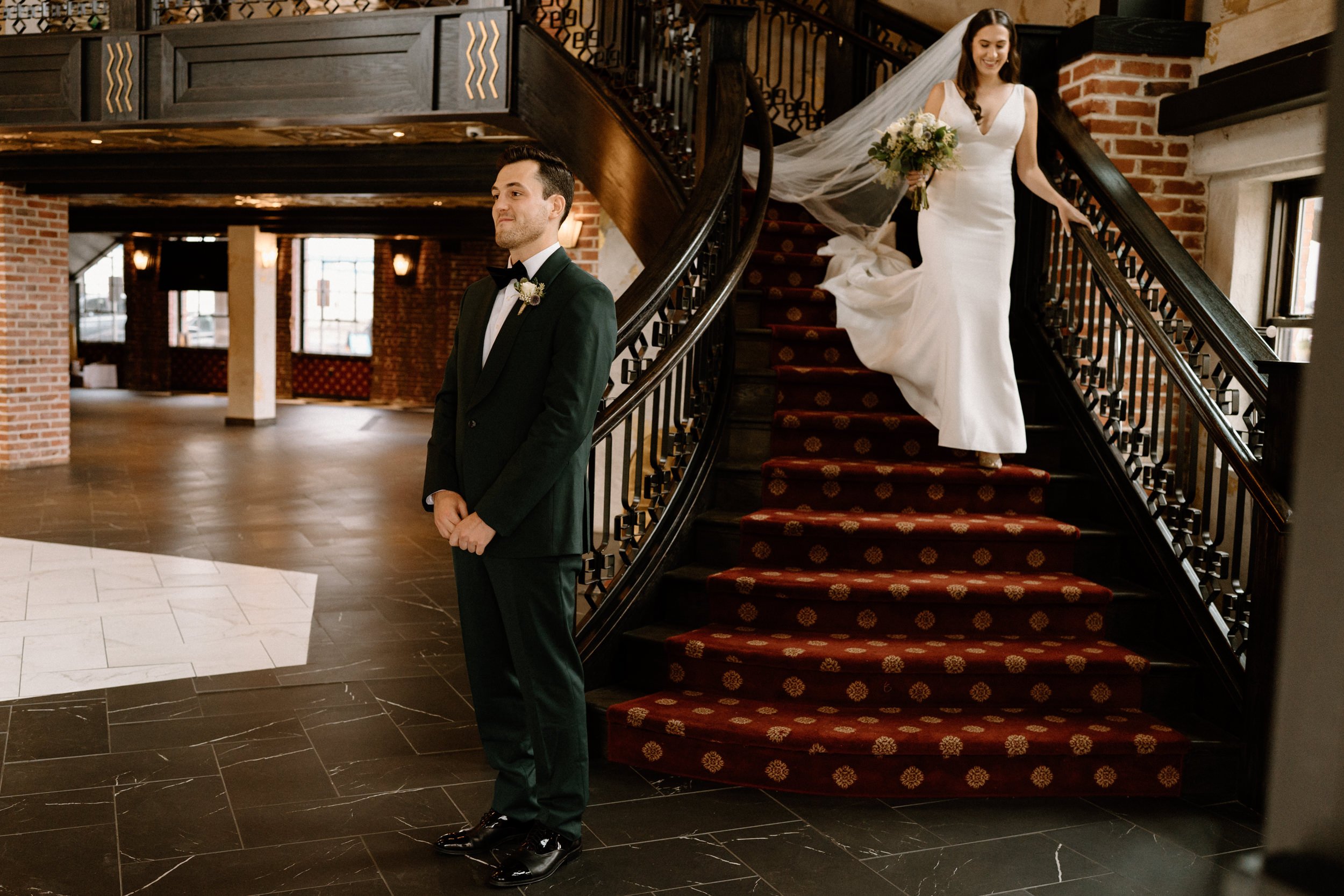 The bride walks down the staircase toward the waiting groom at Ironworks in Denver, CO