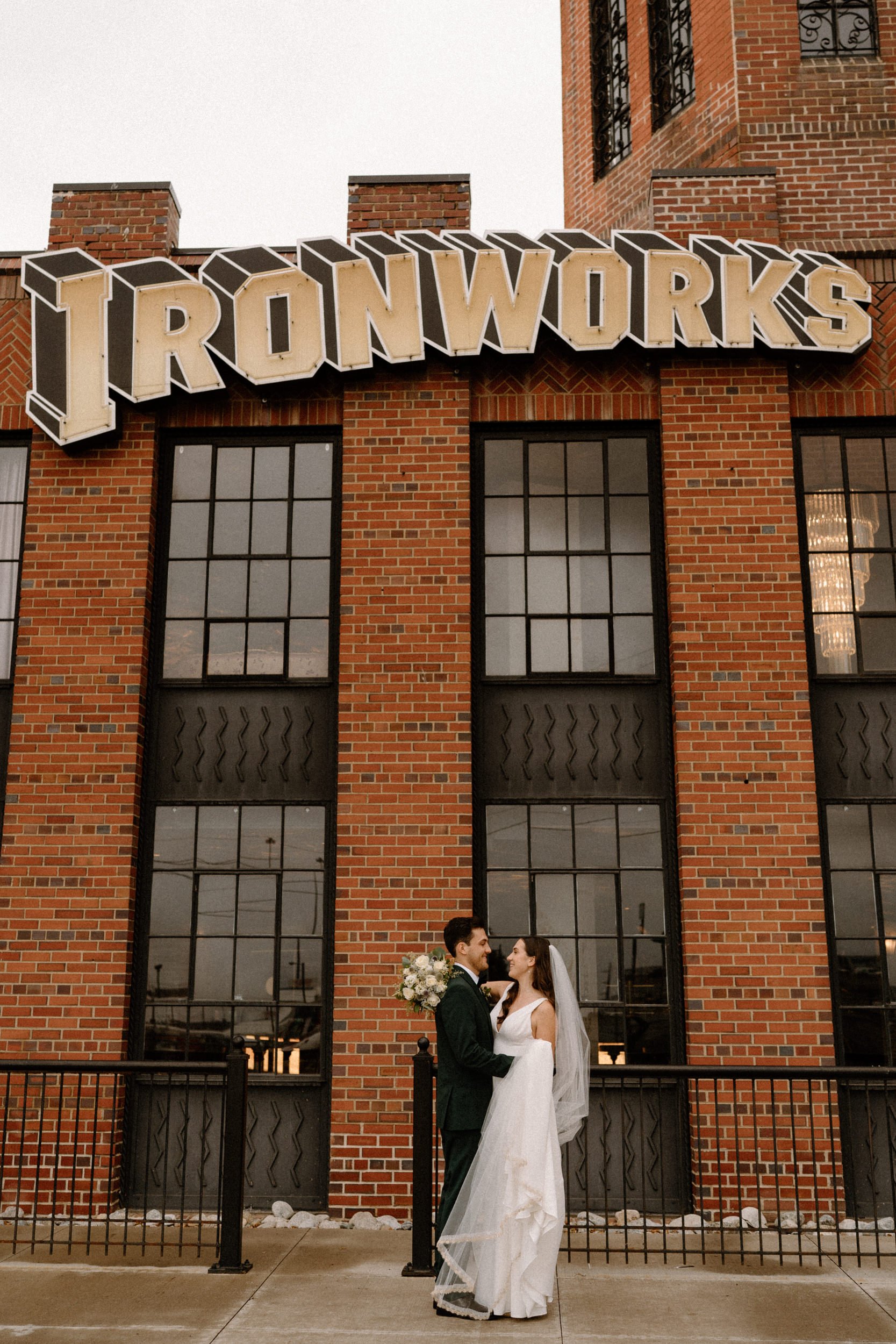 The bride and groom pose against a brick building at Ironworks in Denver, CO