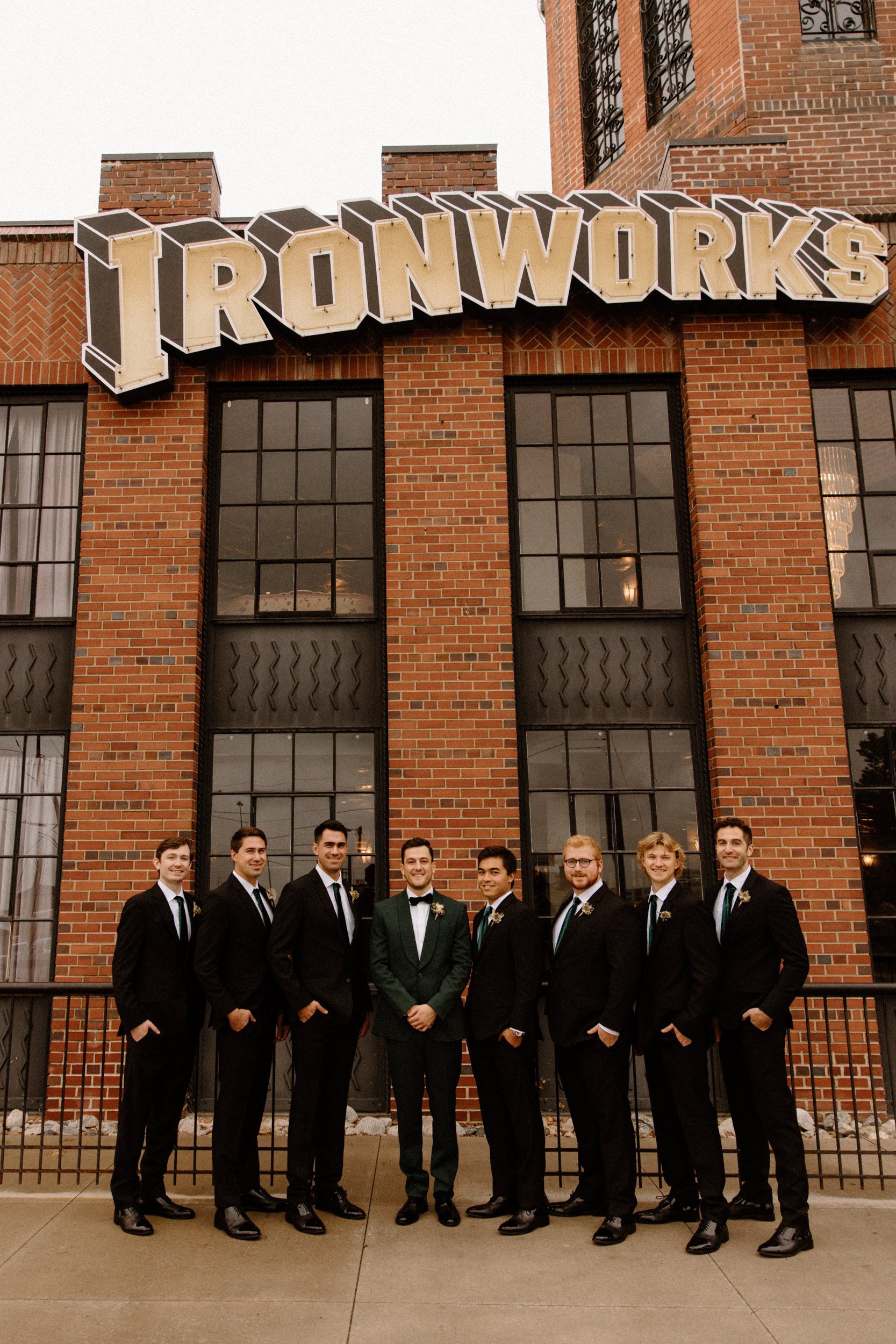 The groom and groomsmen pose under the Ironworks sign