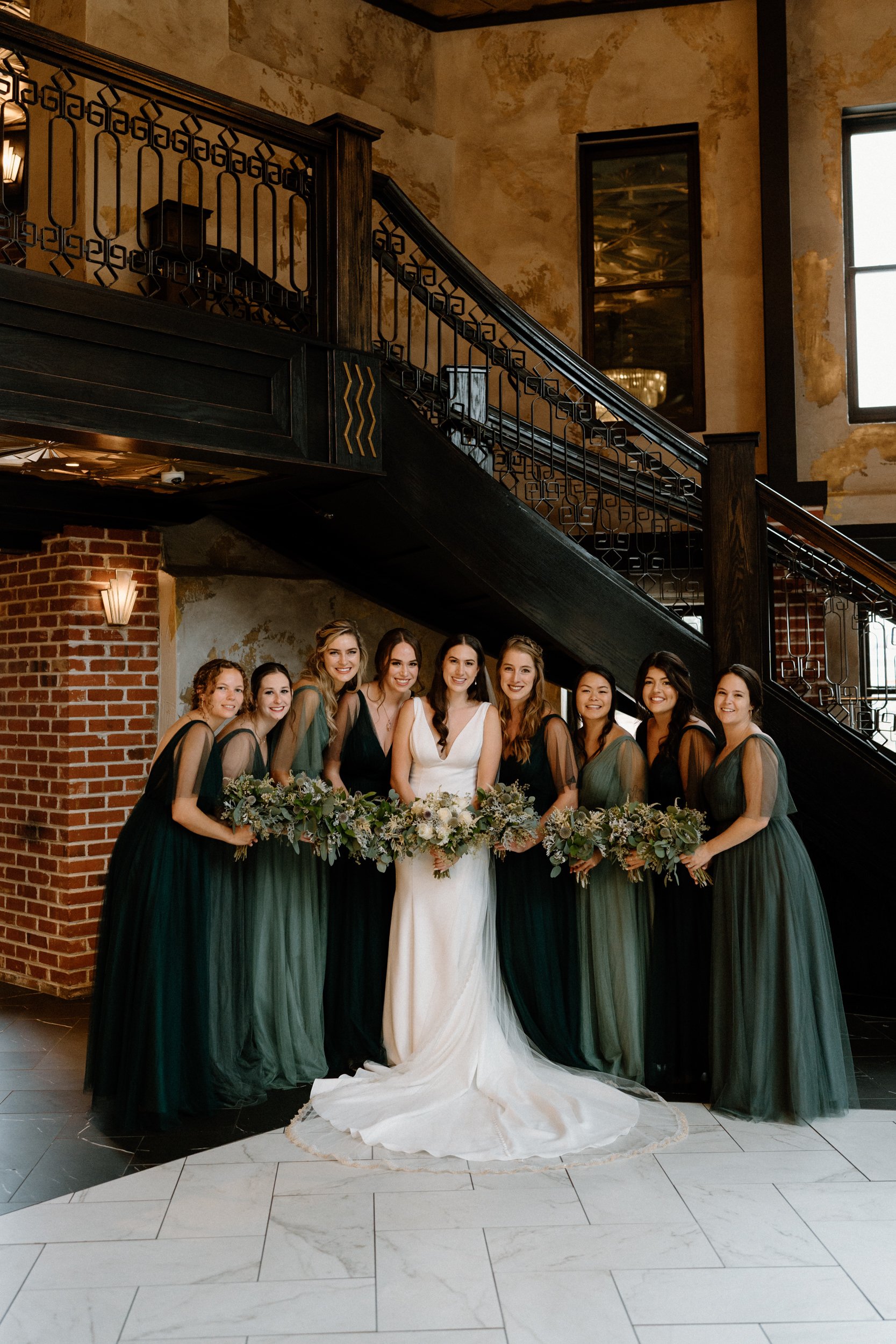 The bride and her bridesmaids pose beneath the staircase at Ironworks in Denver, CO