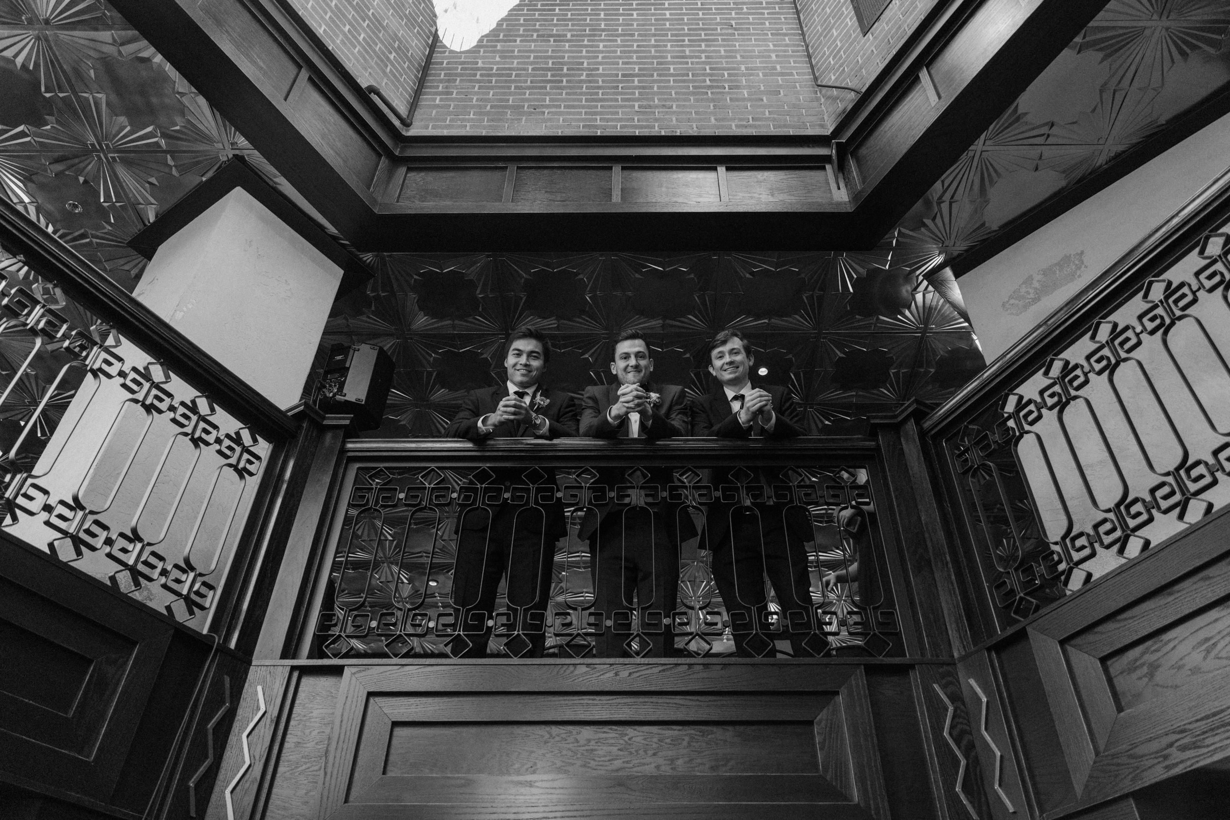 Three groomsmen look down from the lobby of Ironworks in Denver, CO