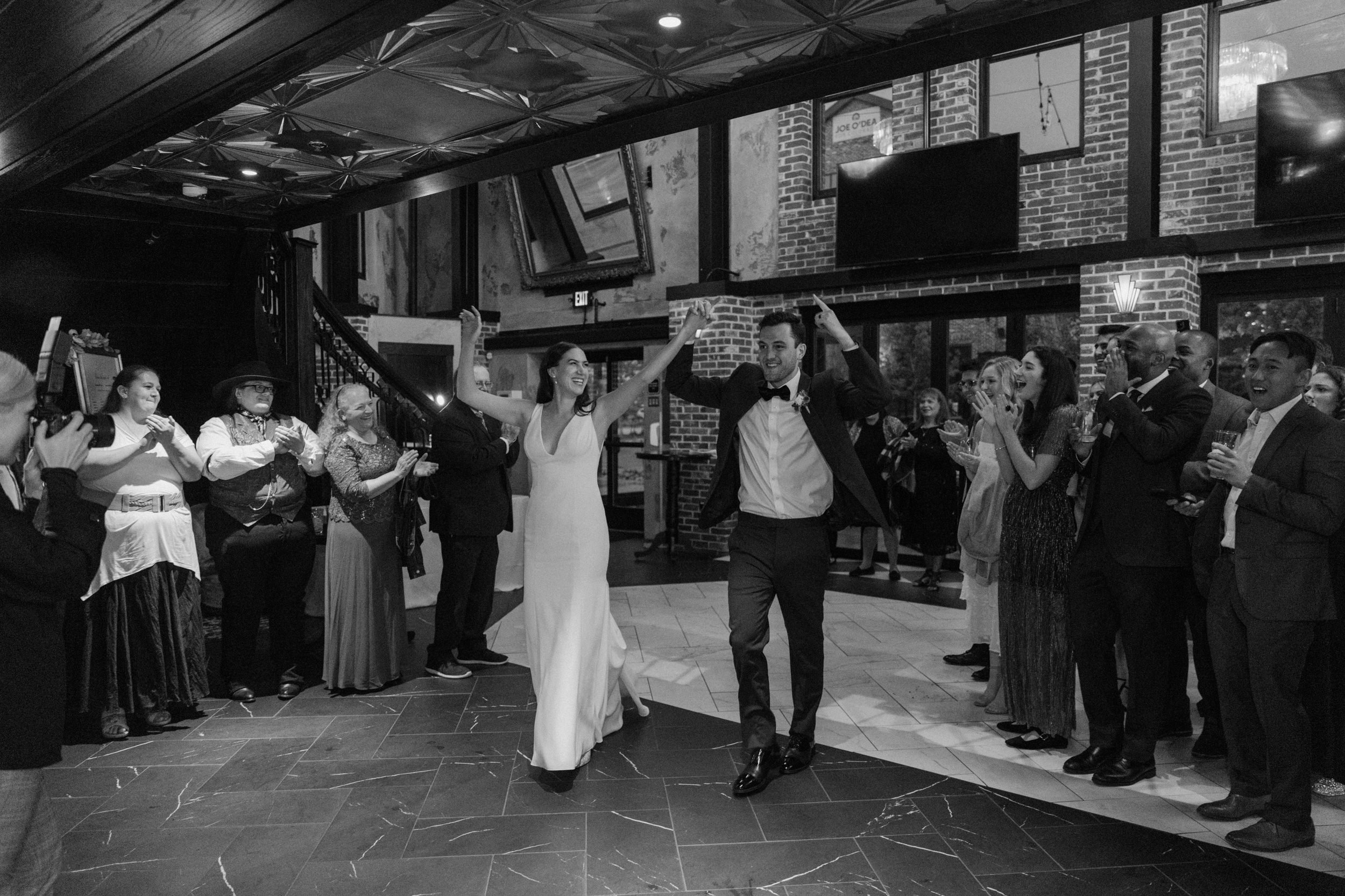 The bride and groom throw their hands in the air as they enter the reception