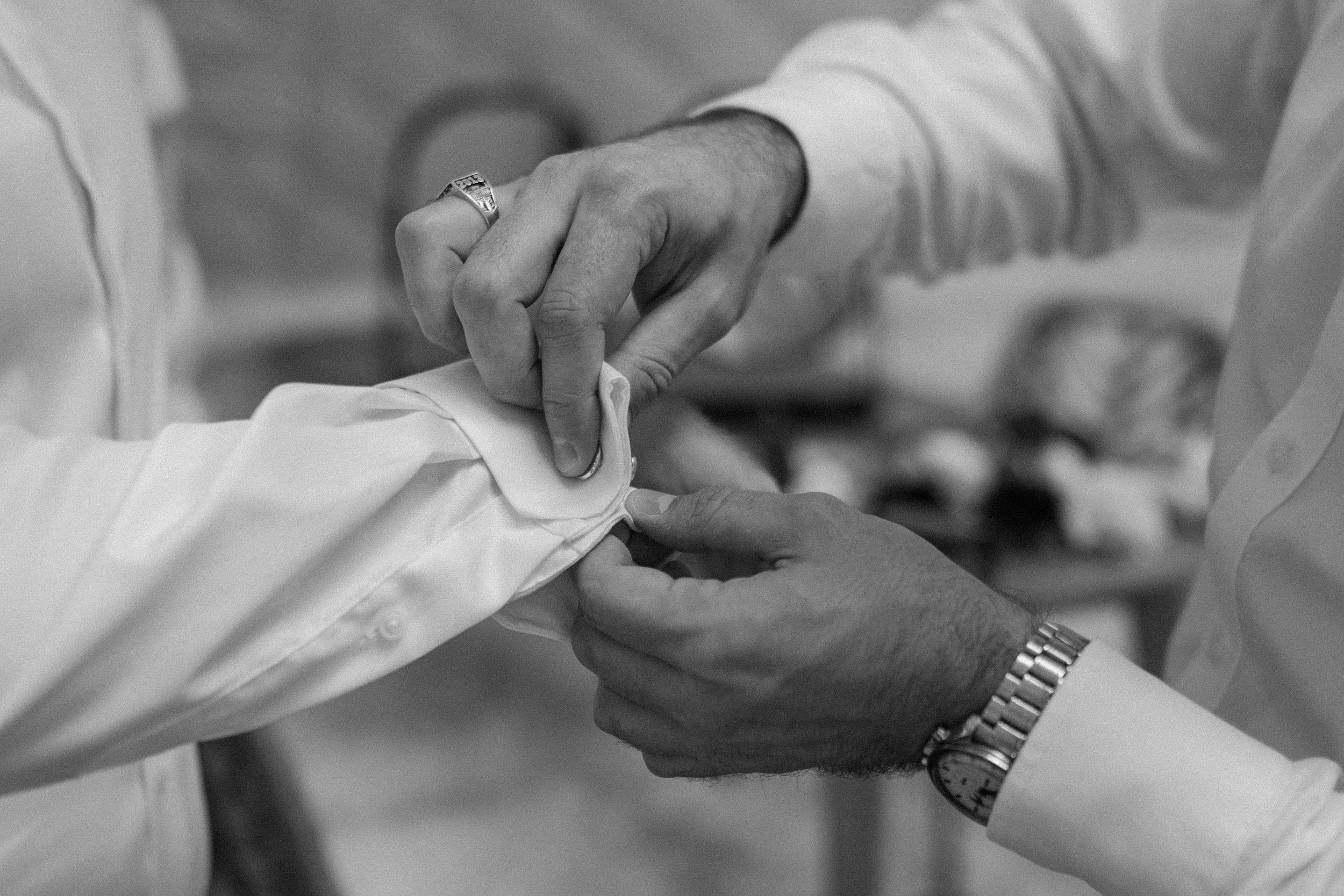 A groomsmen helps the groom with his cufflinks