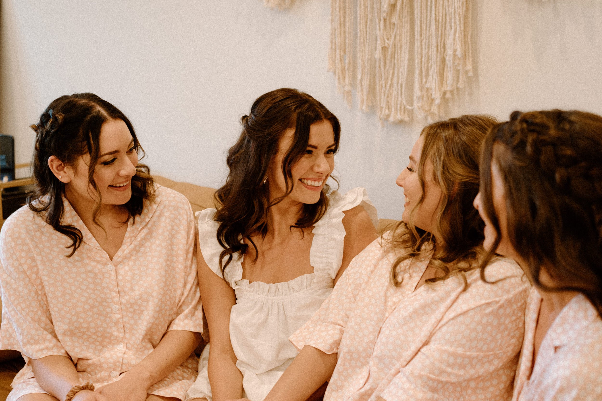 The bride laughs with her bridesmaids as they get ready together