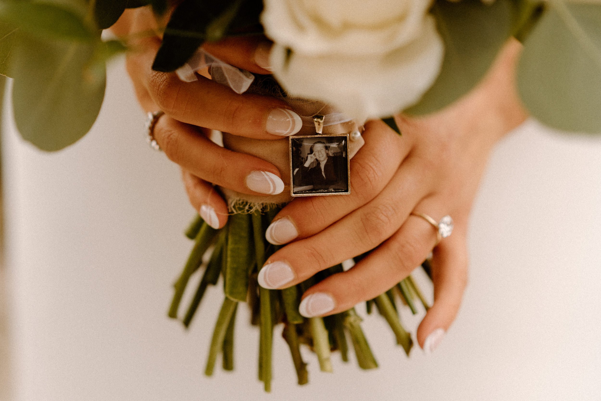 A small photo locket of a man hangs from the bride's bridal bouquet