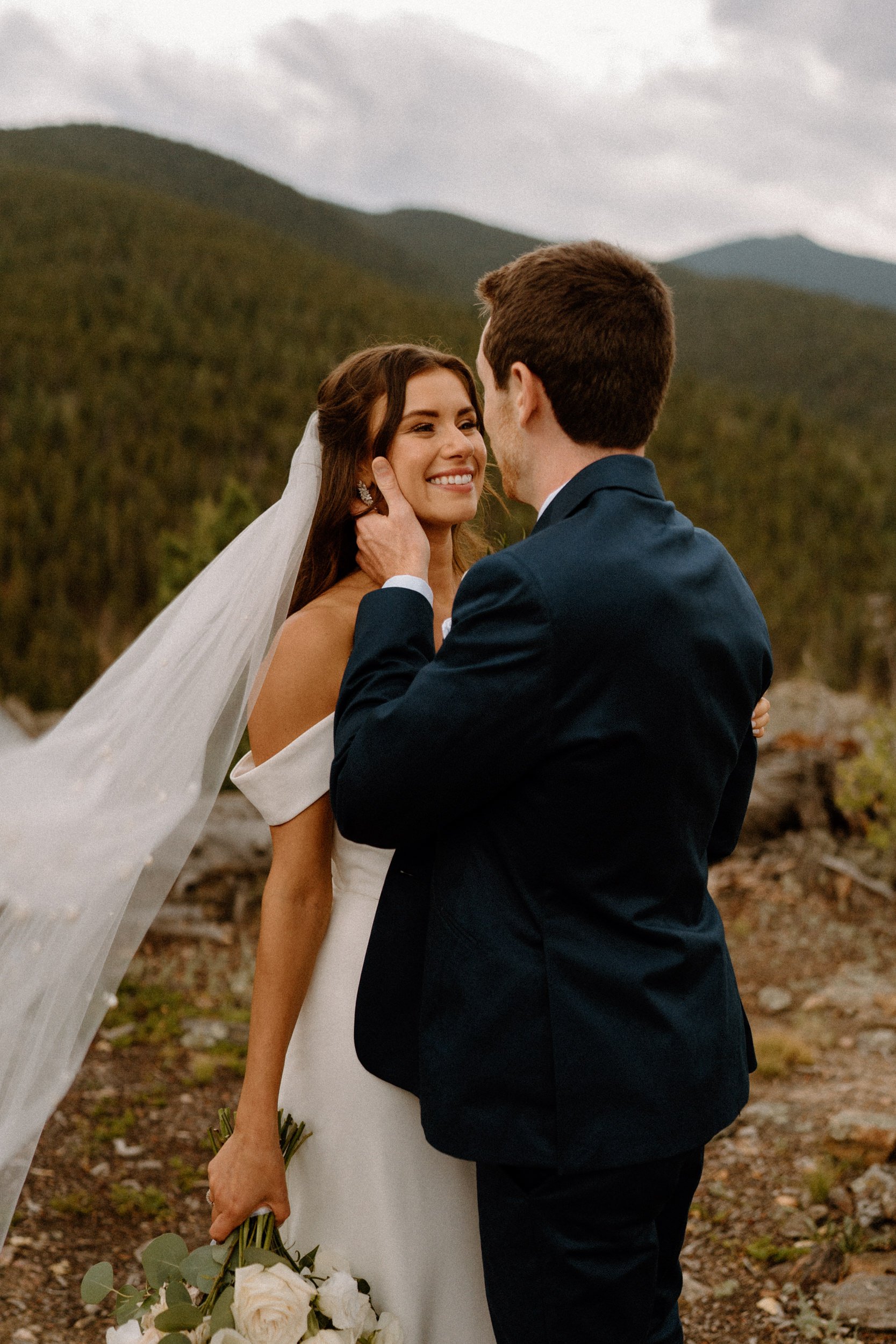 The bride smiles back at the groom as he holds her face at North Star Gatherings in Idaho Springs, CO